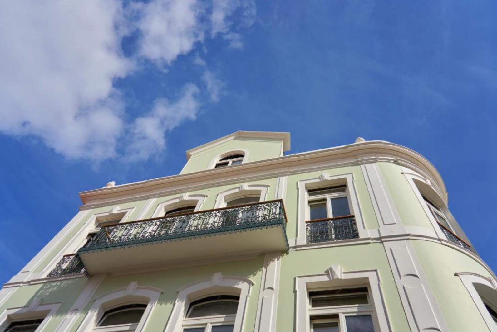 Fachada verde-clara do Hotel Caju no Funchal com varandas de ferro forjado sob o ceu azul.