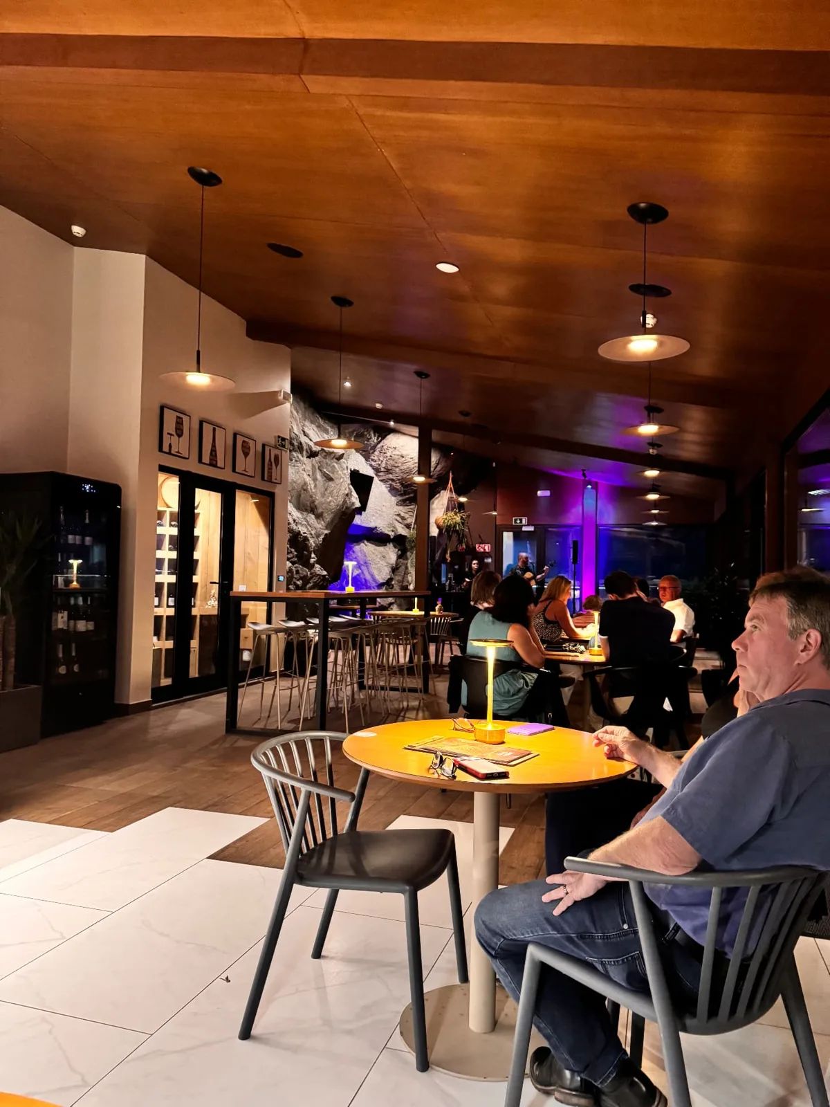 Capoeira Lounge interior in Caniço at night, with a live band, purple stage lighting, timber ceiling and an exposed rock wall