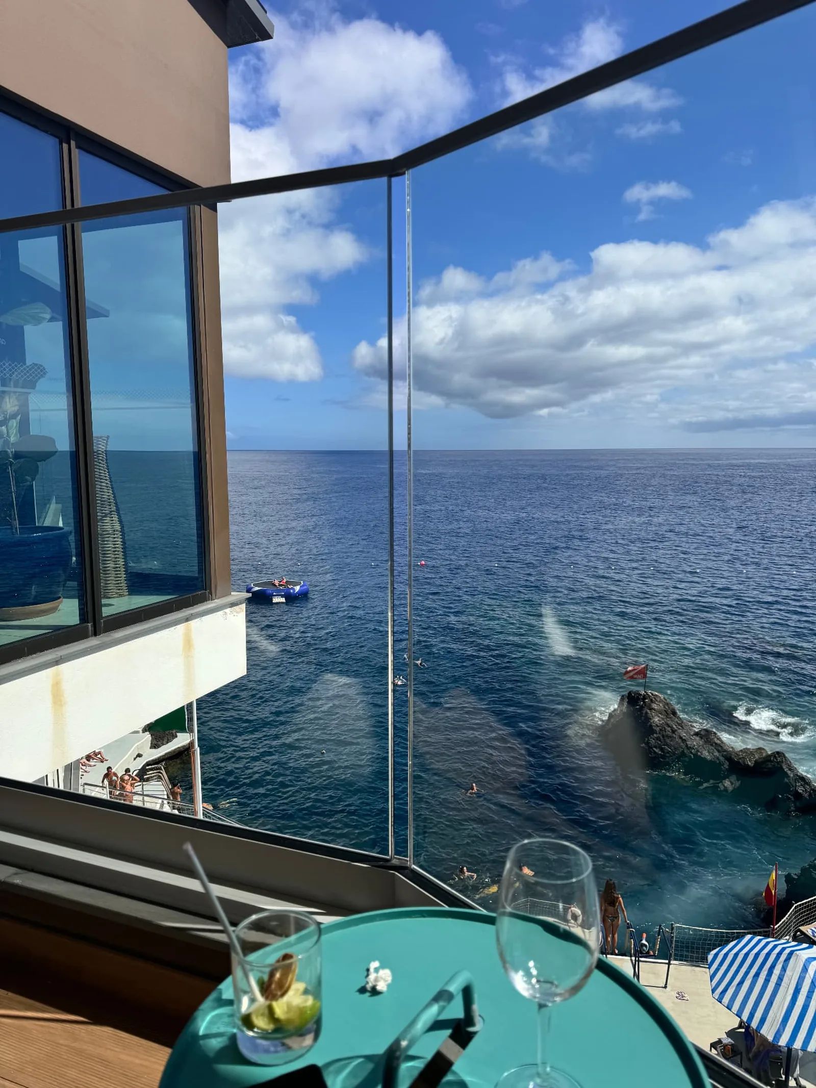 Drinks on a table beside floor-to-ceiling glass at Capoeira Lounge, looking out over the Atlantic and the Caniço de Baixo sea platform
