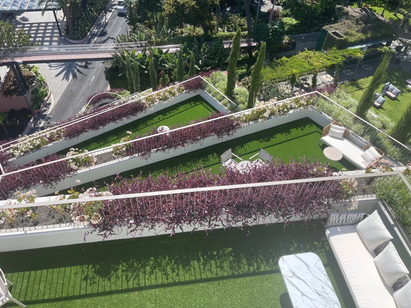 Looking down from Cloud Bar onto the planted rooftop terraces of NEXT Hotel Madeira in Funchal, with lawns, purple planting and white sofas