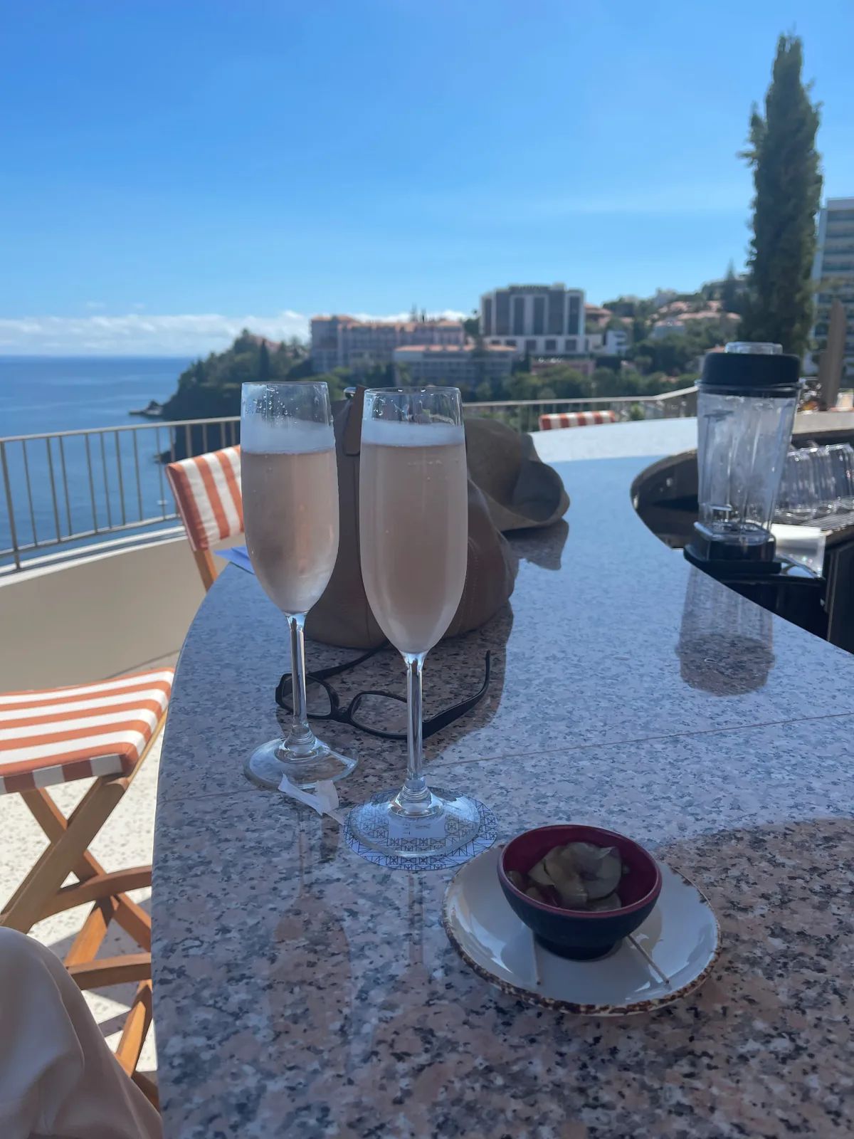 Two glasses of sparkling rose on the granite bar counter at Cloud Bar, NEXT Hotel Madeira, with the Atlantic and Funchal hotel district behind