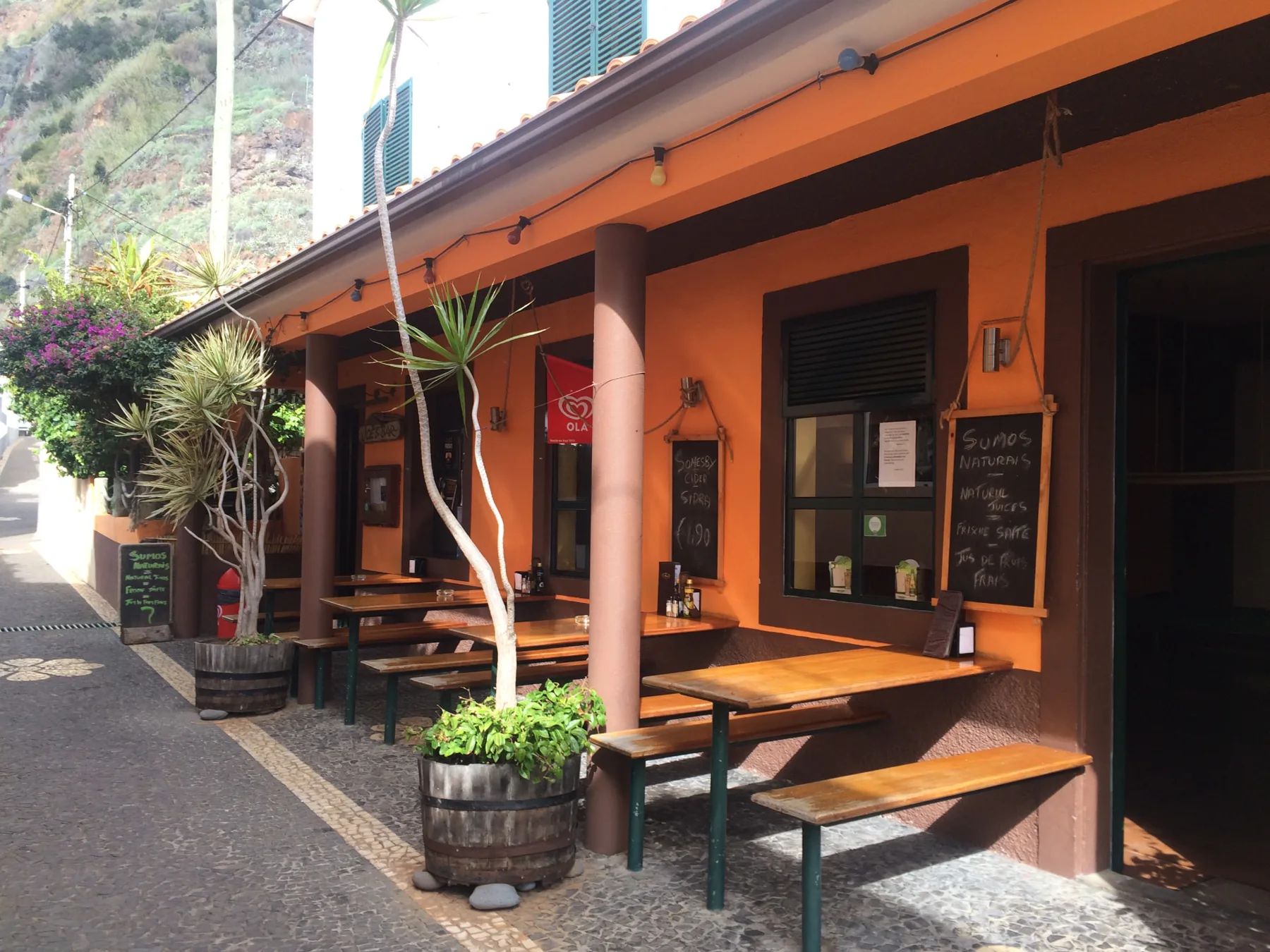 The orange front of Joe's Bar on a cobbled lane in Jardim do Mar, with bench tables on the terrace