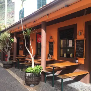 The orange front of Joe's Bar on a cobbled lane in Jardim do Mar, with bench tables on the terrace