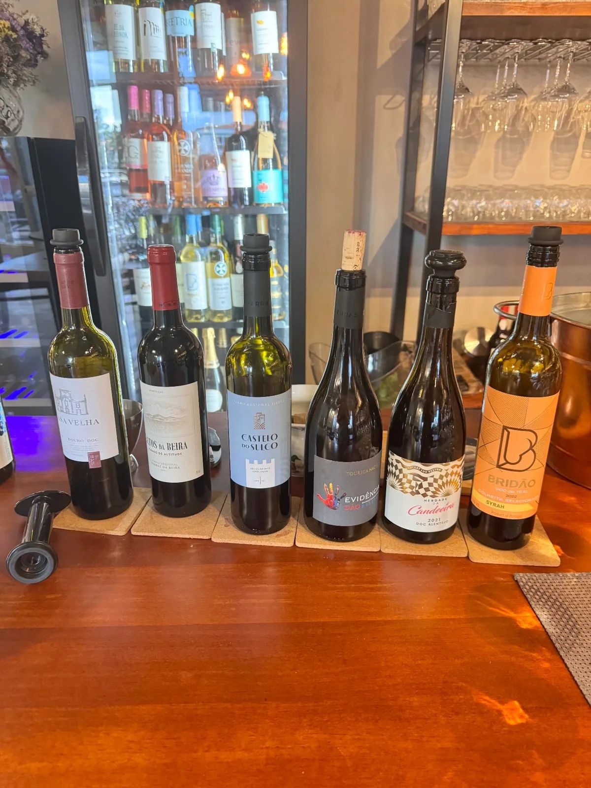 Six open bottles of Portuguese wine lined up on the wooden counter at Just Add Vino