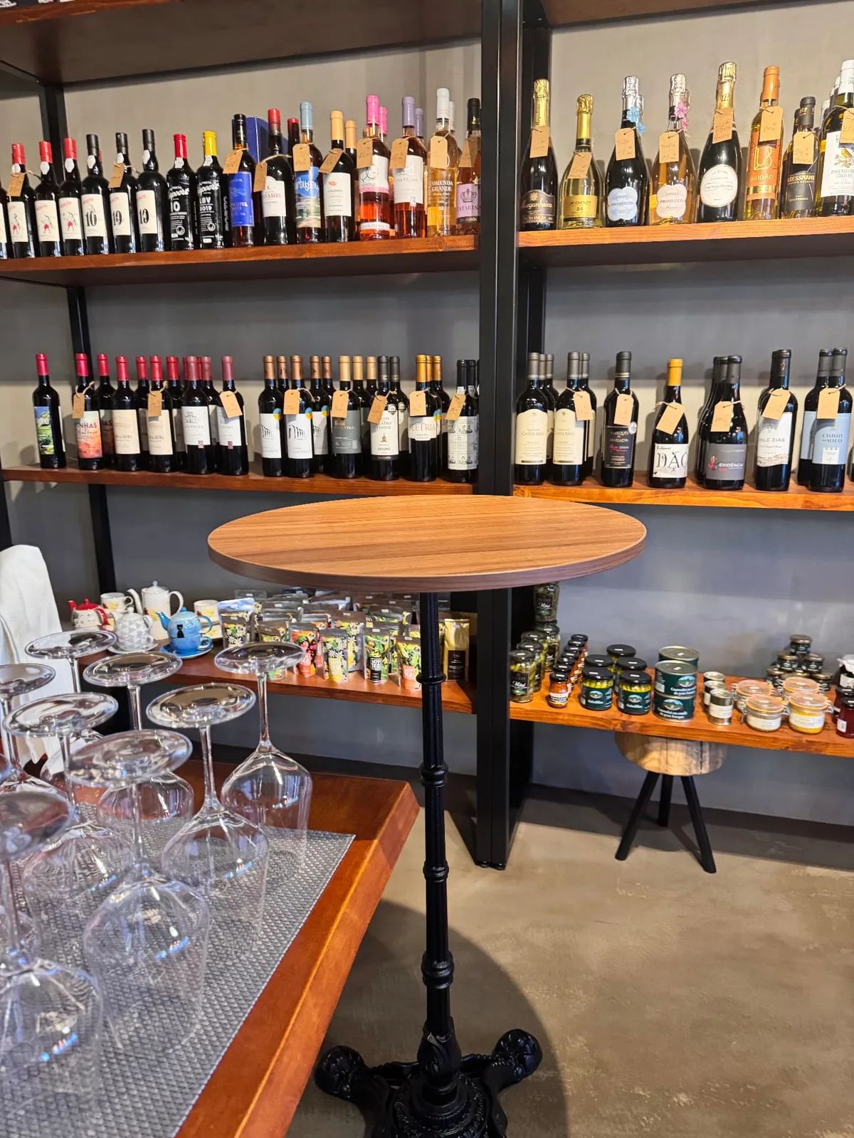 Shelves of Portuguese wines behind a tall wooden tasting table at Just Add Vino in Caniço