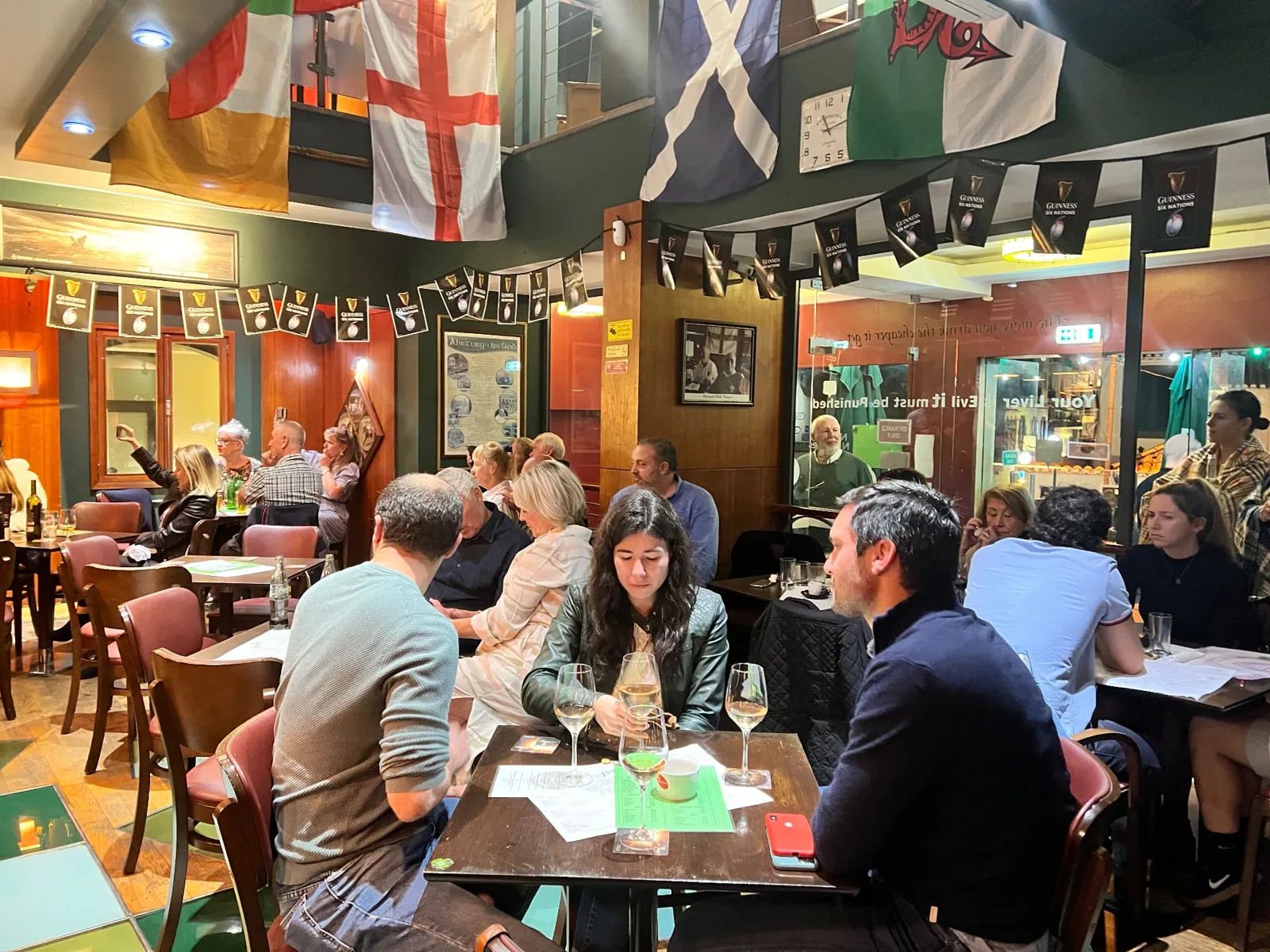 O interior do Moynihans Irish Bar, no Funchal, com bandeiras internacionais penduradas no teto e clientes sentados em mesas de madeira