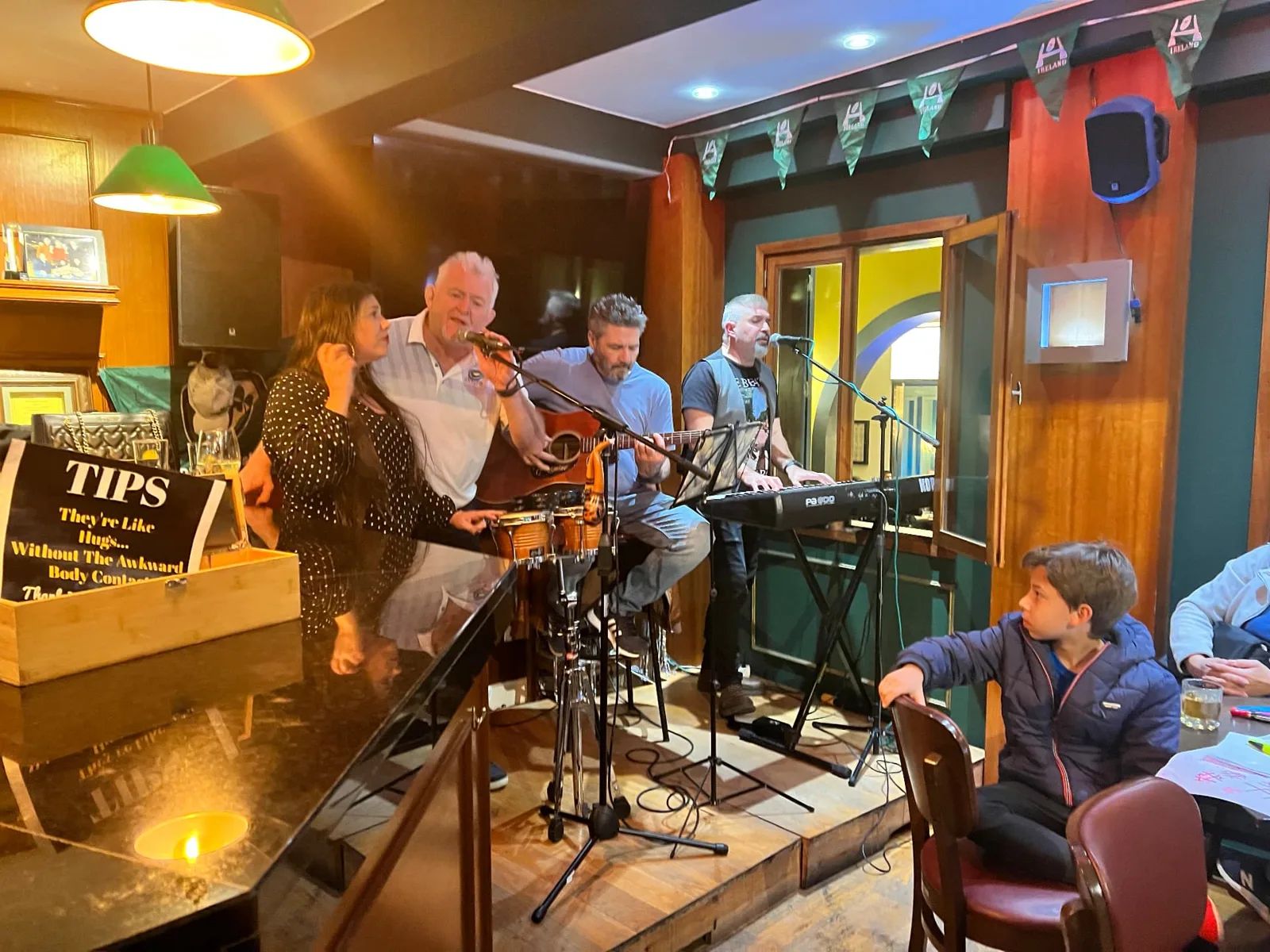 Uma banda ao vivo a atuar no pequeno palco do Moynihans Irish Bar, no Funchal, com guitarra, teclados e uma caixa de gorjetas em cima do piano
