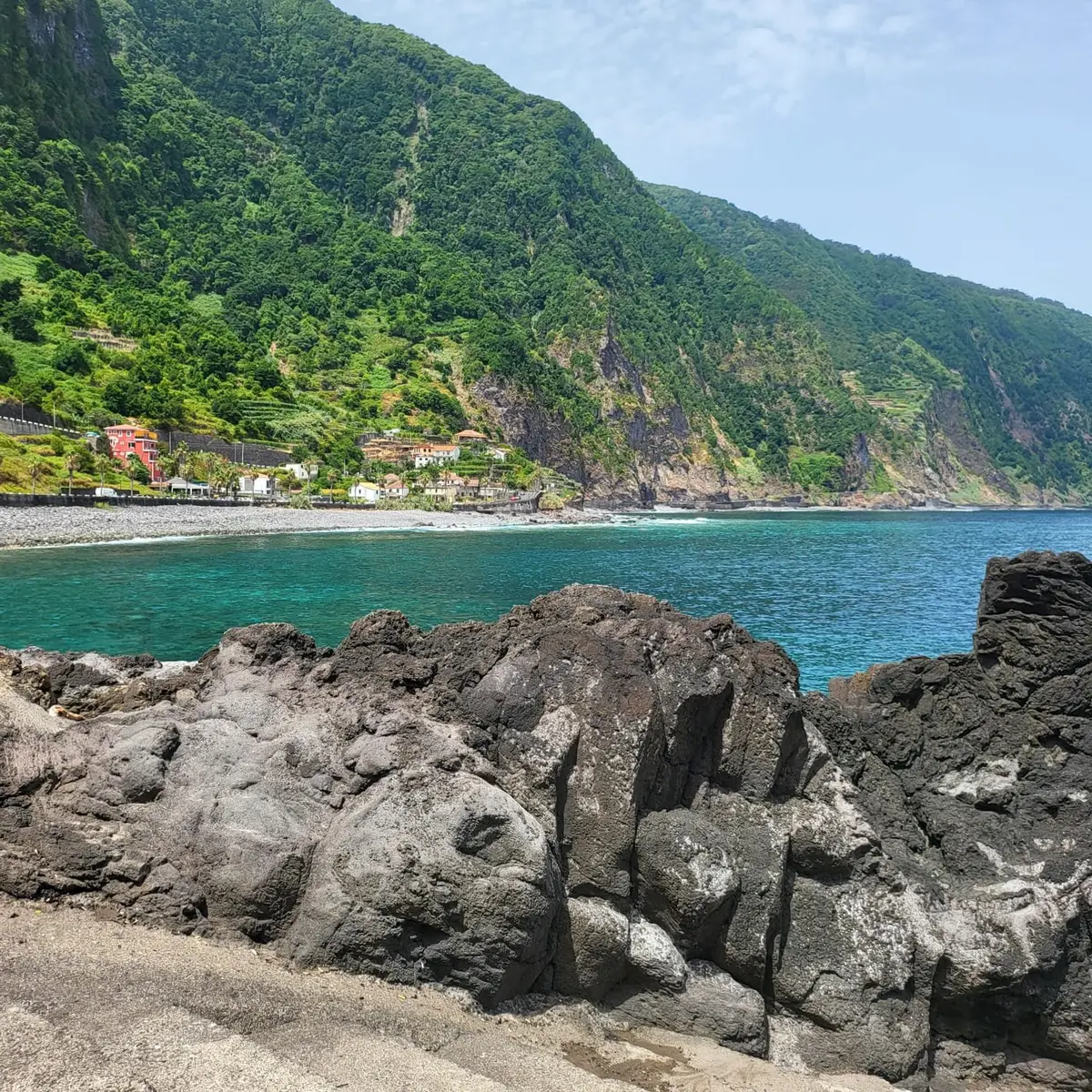 Seixal beach and the green volcanic cliffs of Madeira's north coast seen from the lava rocks at Praia da Laje