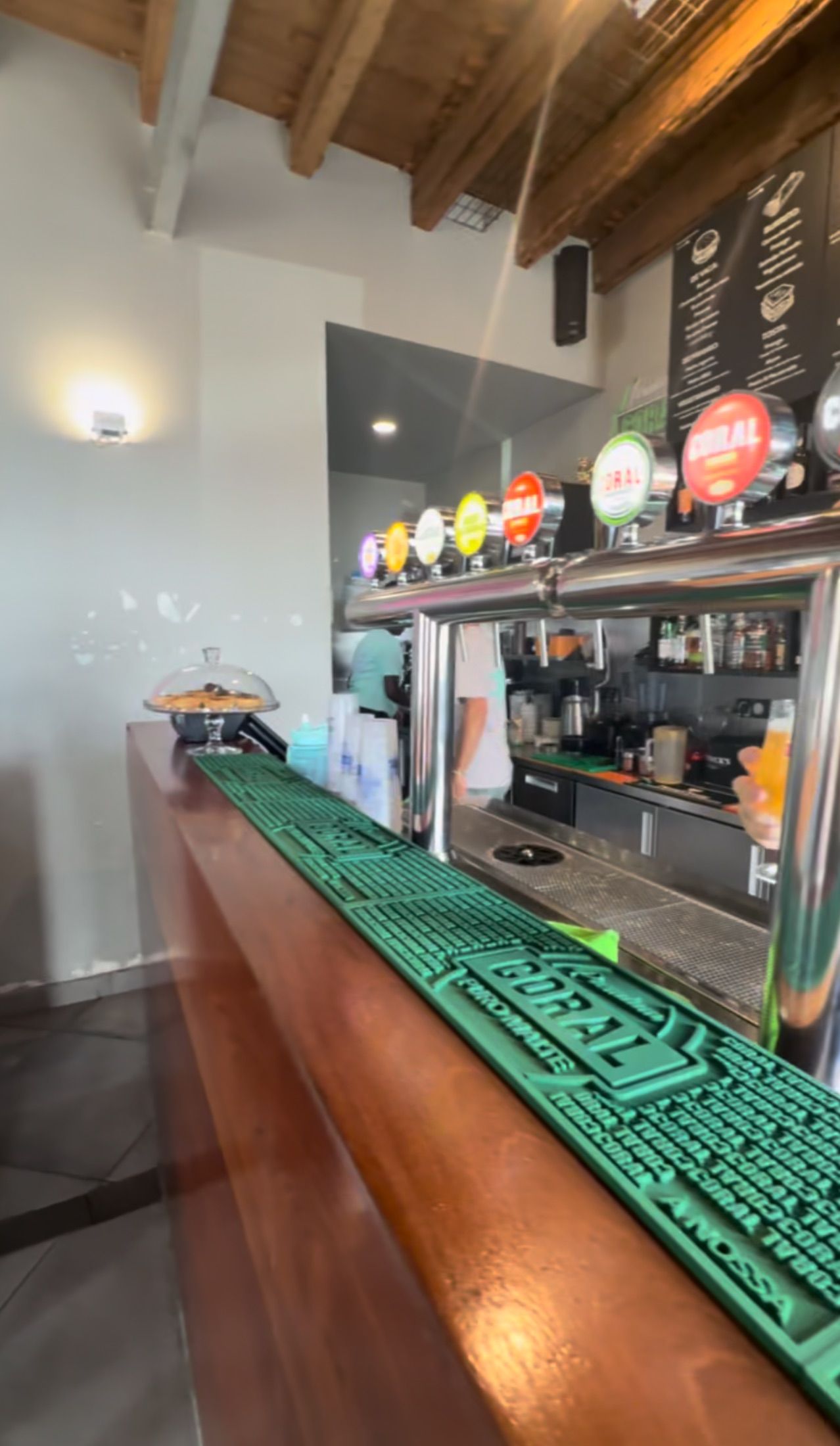 Balcão de madeira com torneiras de cerveja, tapetes verdes Coral e vigas expostas no teto