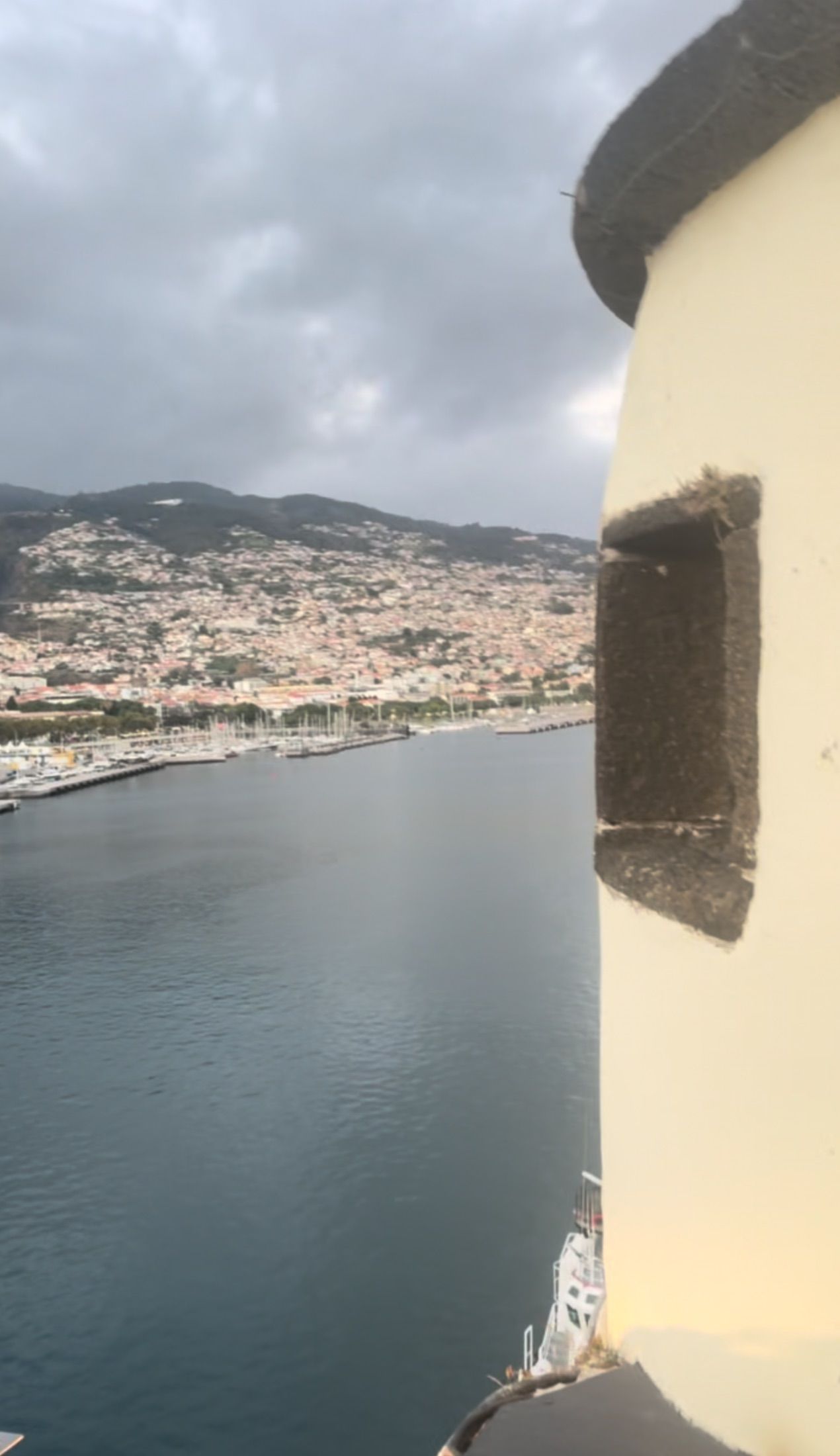 Porto e edifícios na encosta junto a uma parede amarela curva com cantaria escura