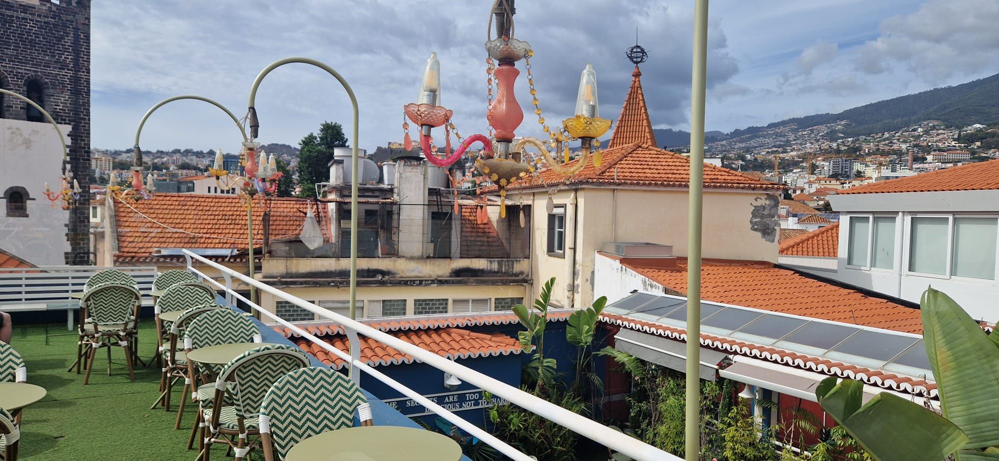 Terraço na cobertura com cadeiras estampadas, lustres coloridos e vista sobre telhados e colinas