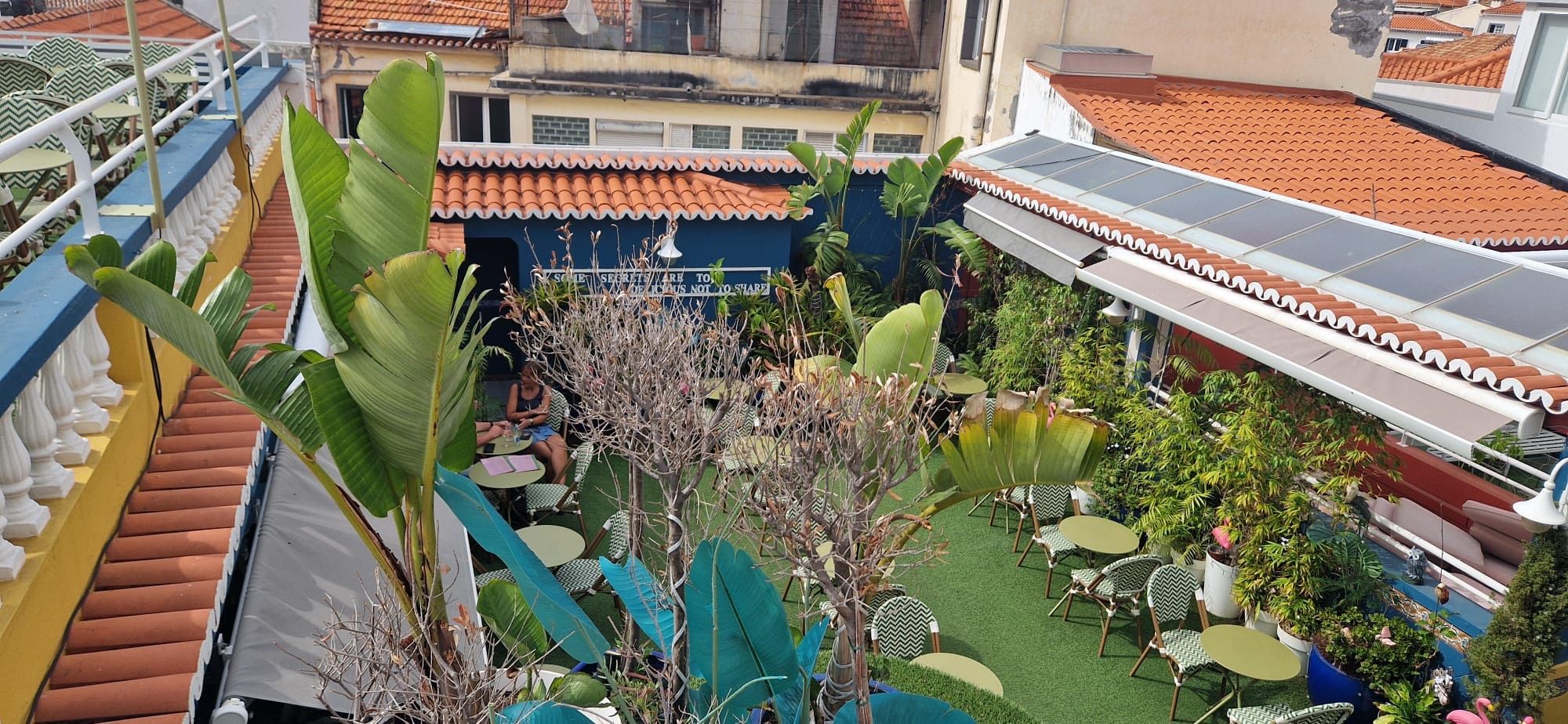Terrace with patterned chairs, round tables and tall plants surrounded by tiled roofs