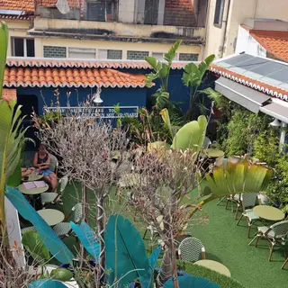 Terrace with patterned chairs, round tables and tall plants surrounded by tiled roofs