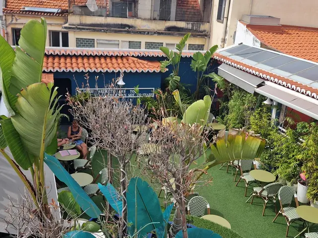 Terrace with patterned chairs, round tables and tall plants surrounded by tiled roofs