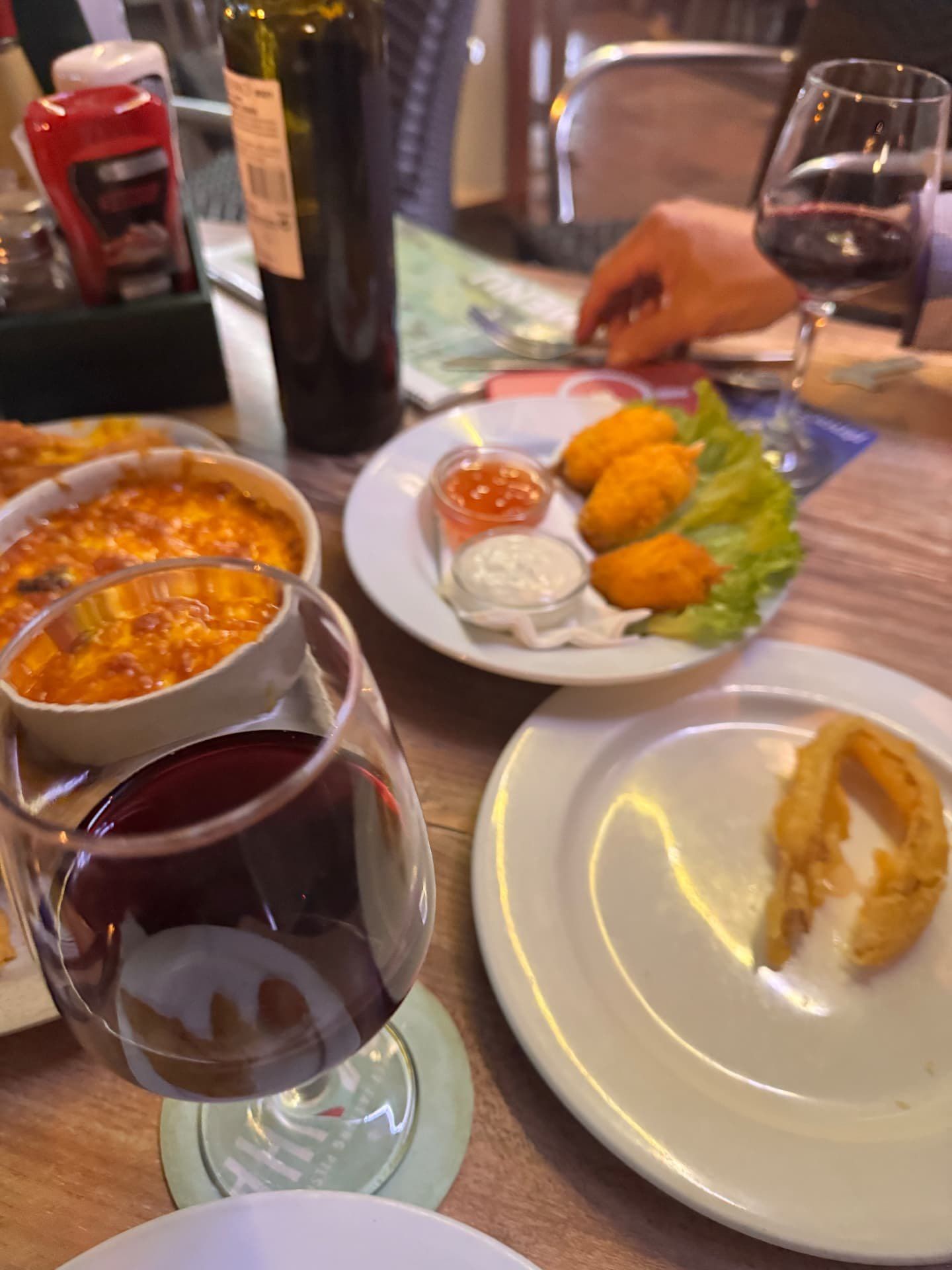 Mesa de jantar partilhada no Moynihan's Irish Bar, no Funchal, na Madeira, com croquetes dourados, molhos para acompanhar, um prato de queijo gratinado e copos de vinho tinto