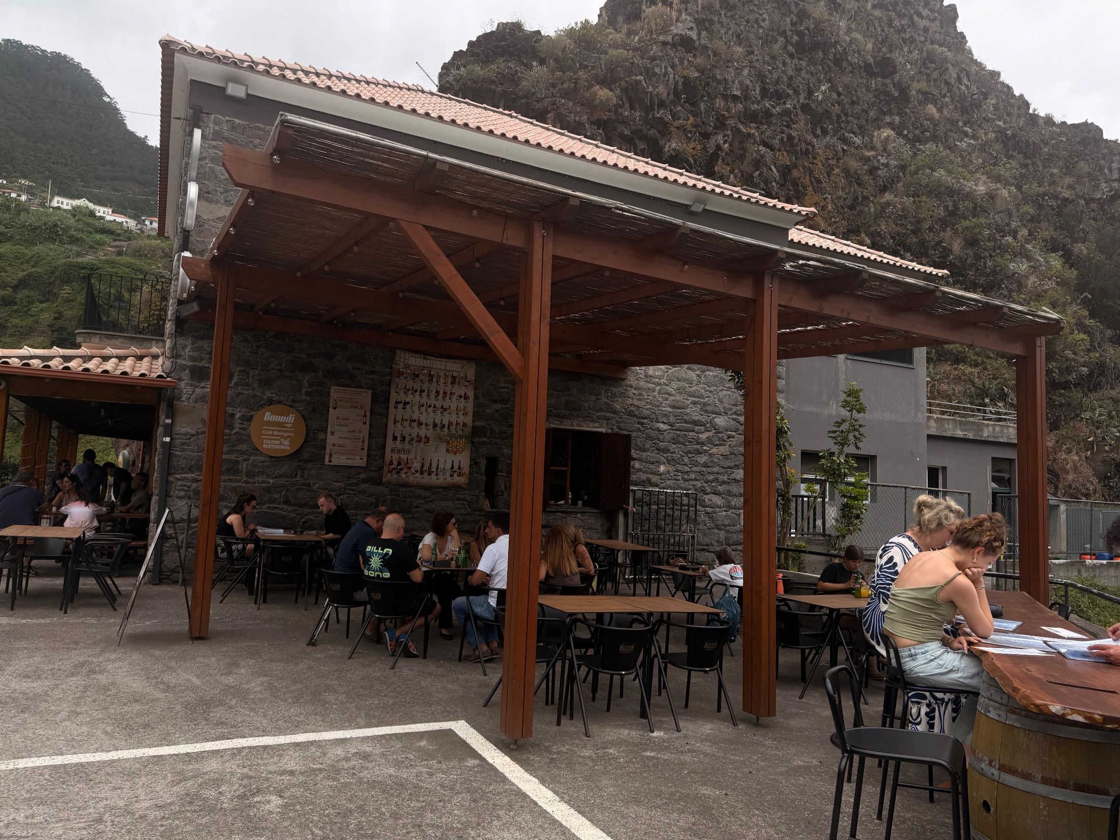 Clientes sentados sob uma pérgula de madeira num bar de pedra junto a uma escarpa