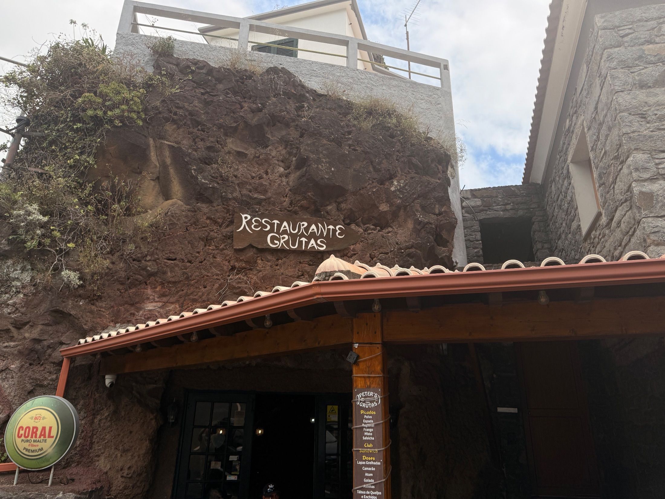 Letreiro do Restaurante Grutas na rocha exposta, acima de um alpendre e da entrada