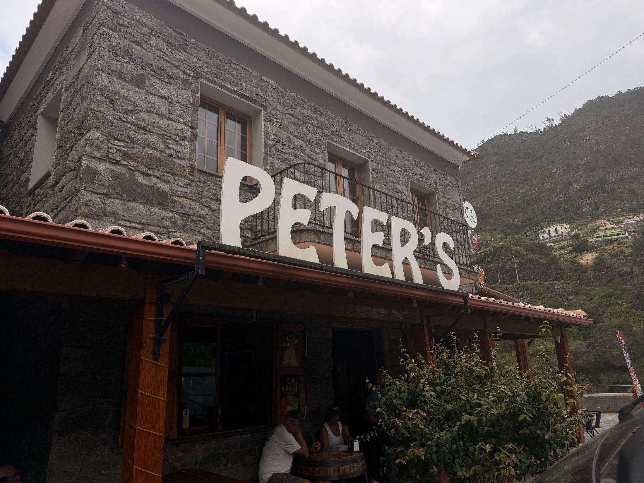Letreiro Peter’s sobre a fachada de pedra de um bar com esplanada coberta