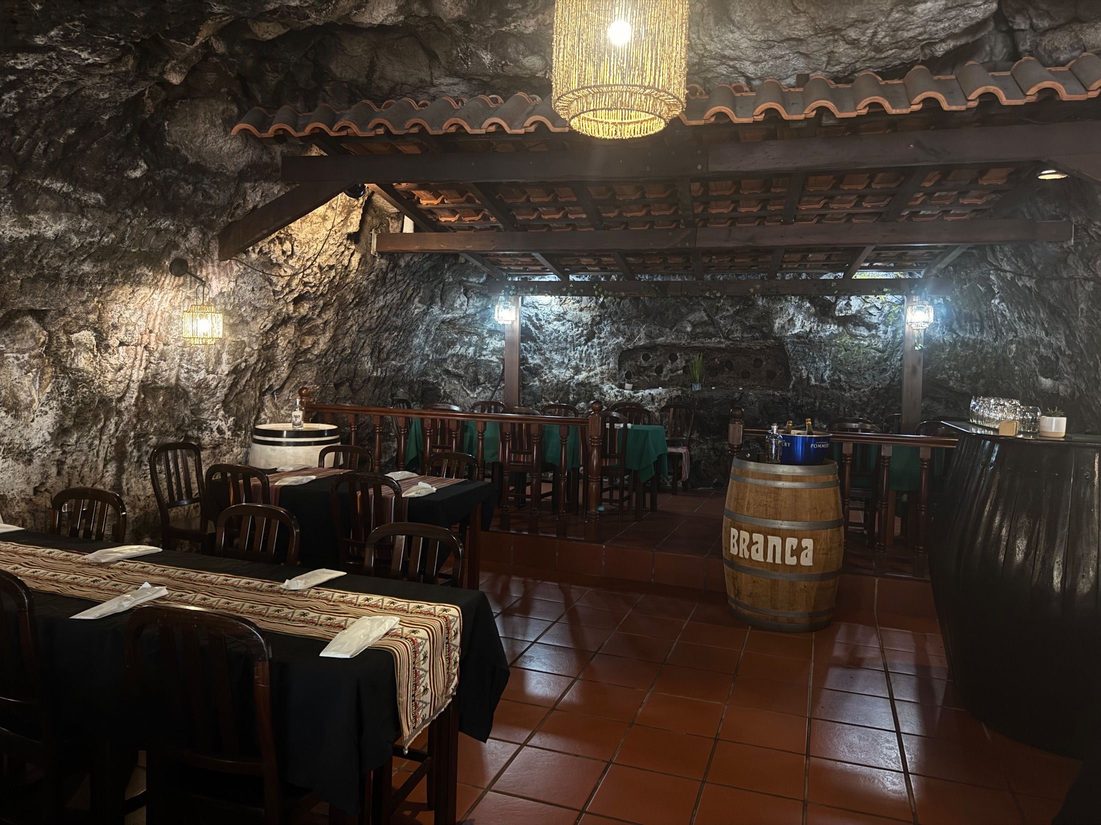 Bar interior with exposed rock walls, wooden chairs, set tables and hanging lamps