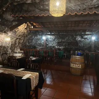 Bar interior with exposed rock walls, wooden chairs, set tables and hanging lamps