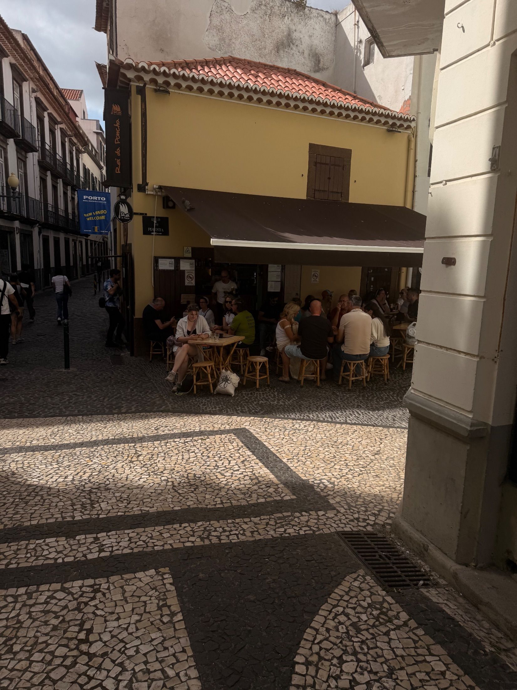 Customers seated beneath a brown awning outside the yellow Rei da Poncha bar