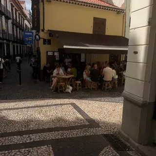 Customers seated beneath a brown awning outside the yellow Rei da Poncha bar