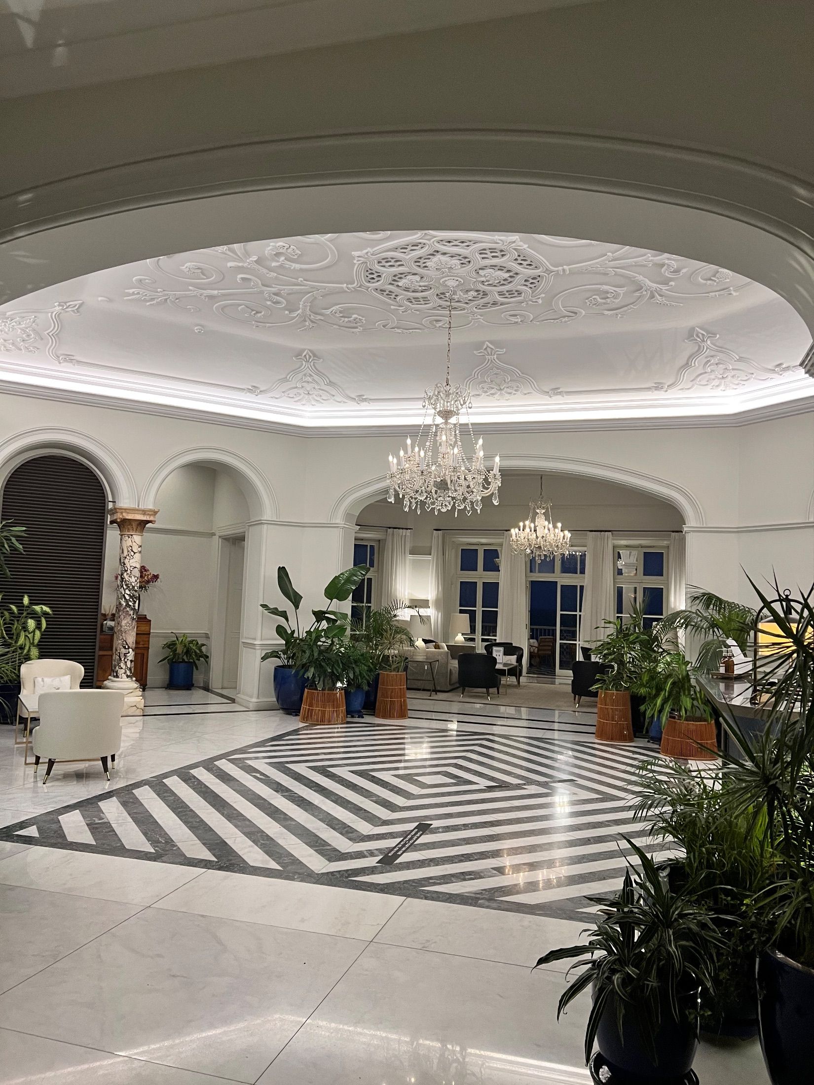 Lounge interior with chandeliers, decorative plaster ceiling, potted plants and geometric floor patterns