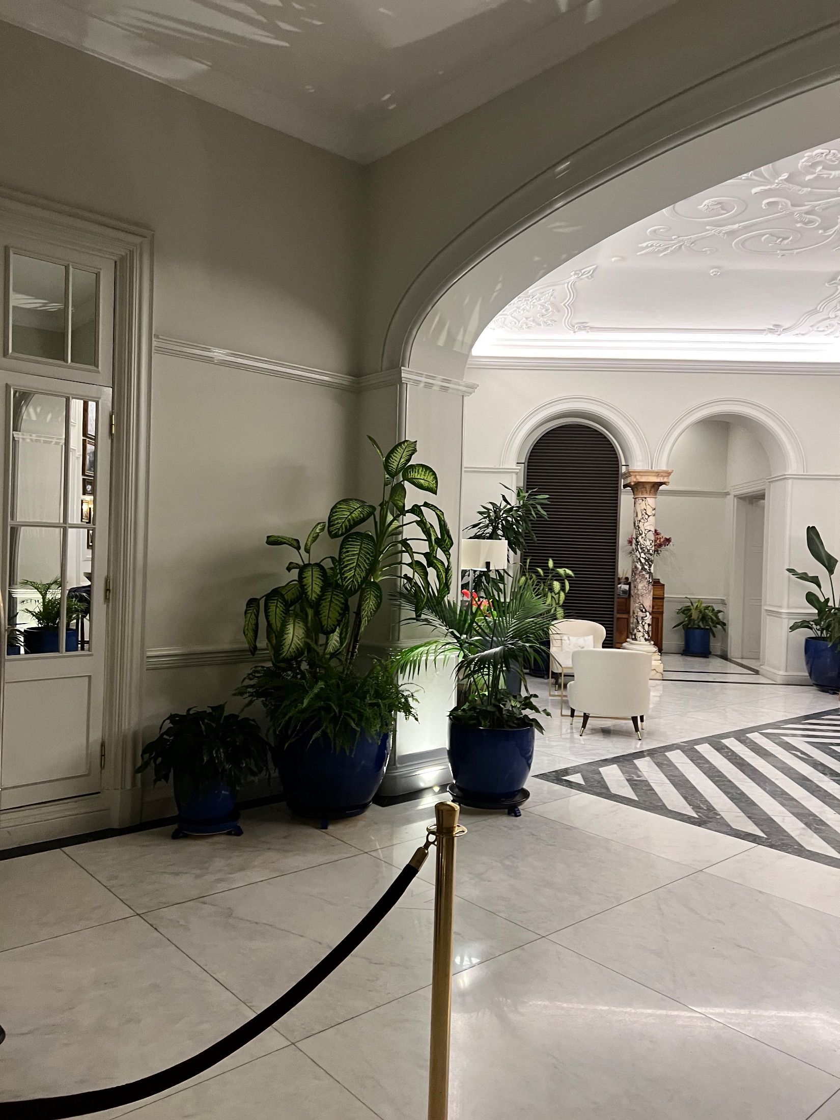 Arched interior with potted plants, white armchairs and a patterned marble floor