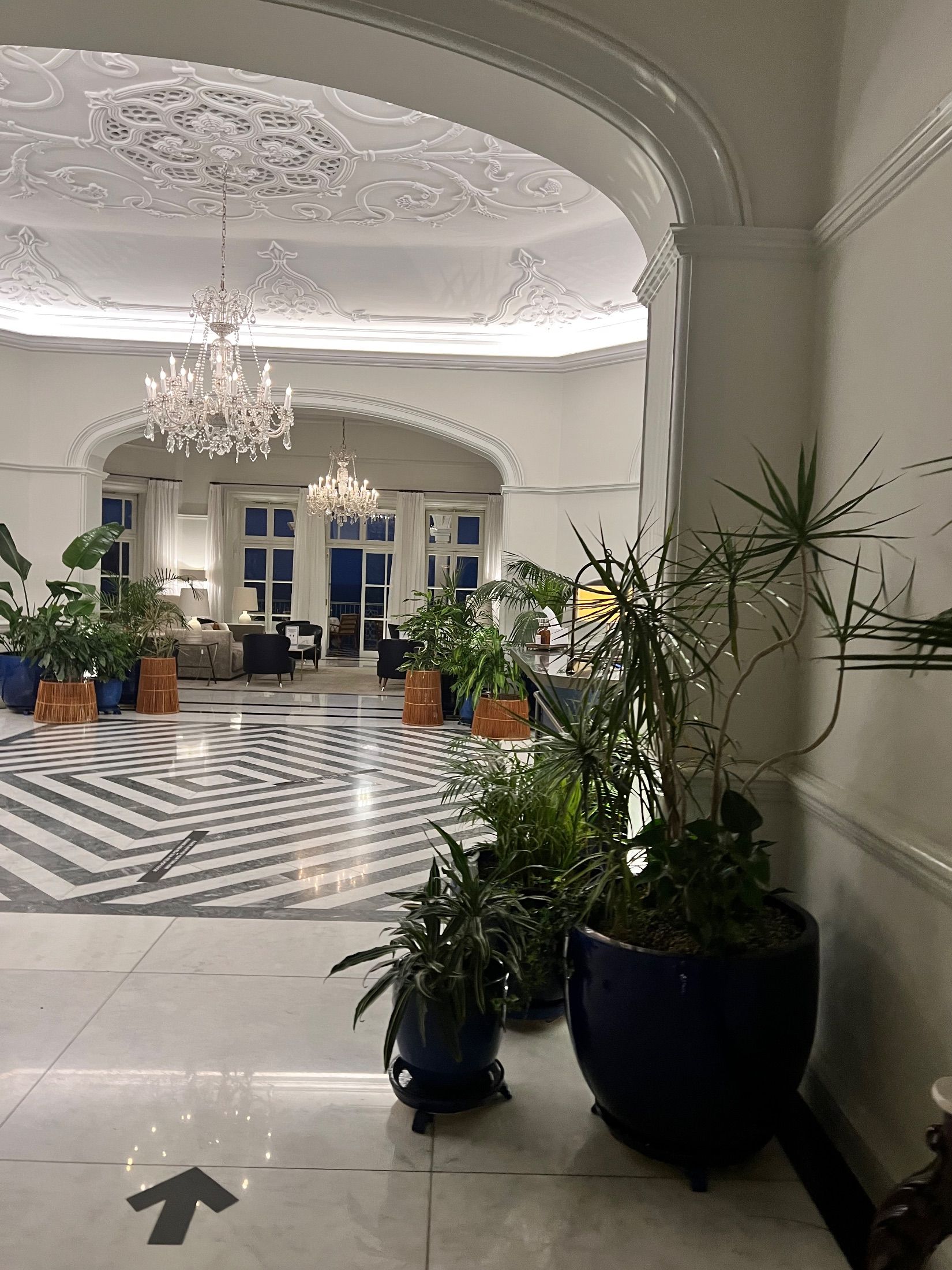 Lounge interior with chandeliers, decorative plasterwork, potted plants and a geometric patterned floor