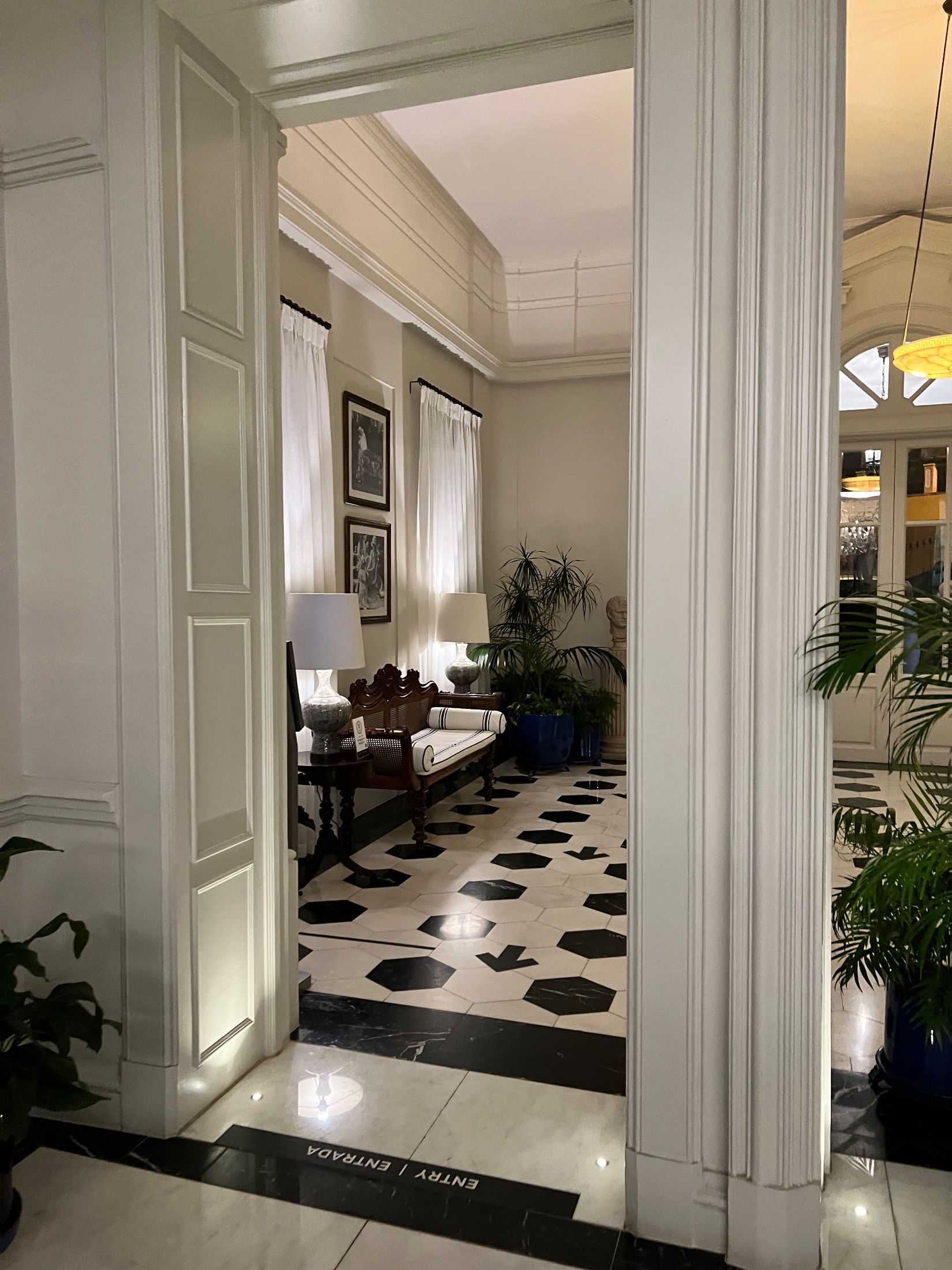 Panelled entrance hall with a wooden bench, potted plants and black-and-white tiled floor