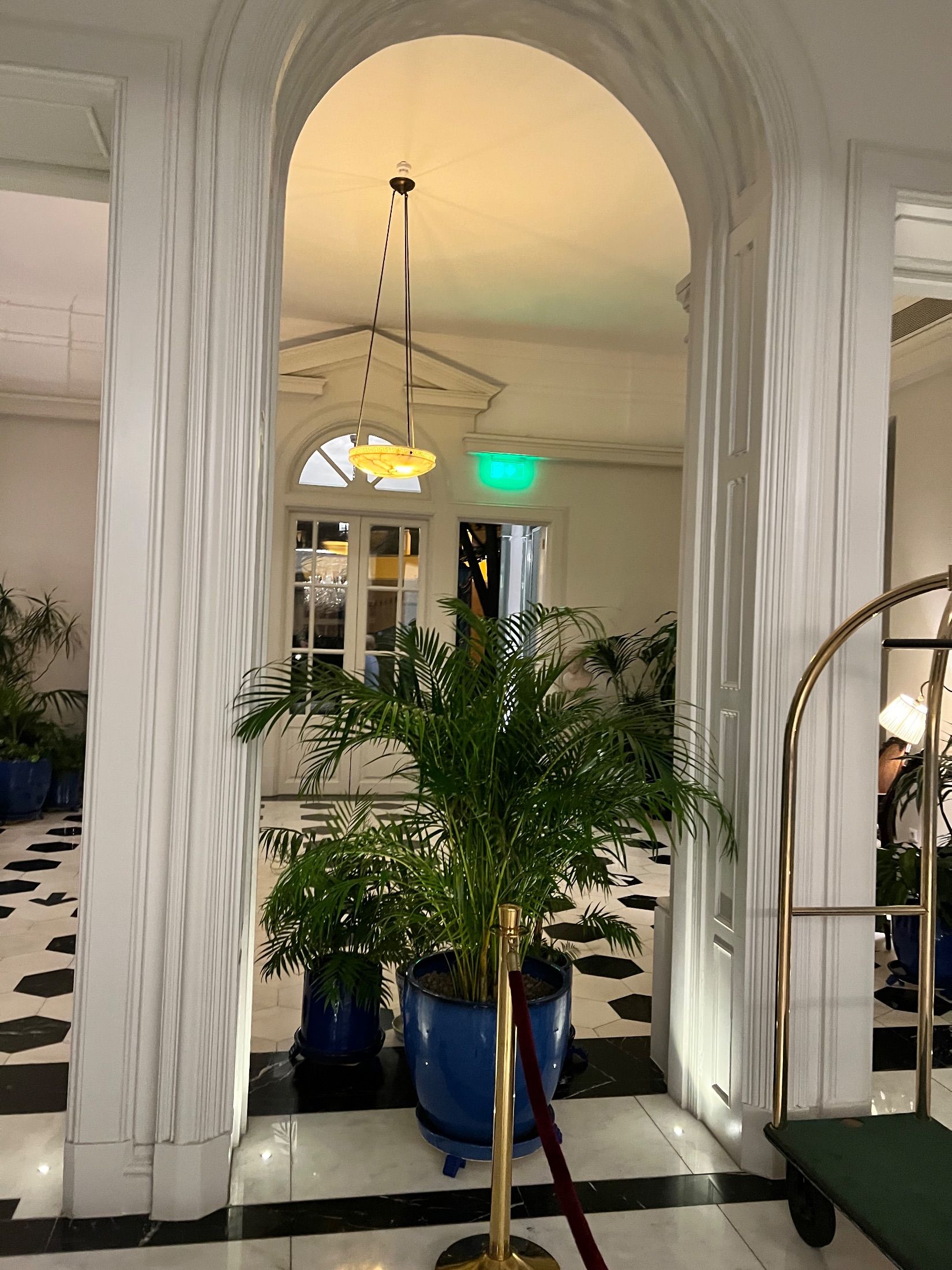 White archway framing palms in blue pots above a black and white tiled floor