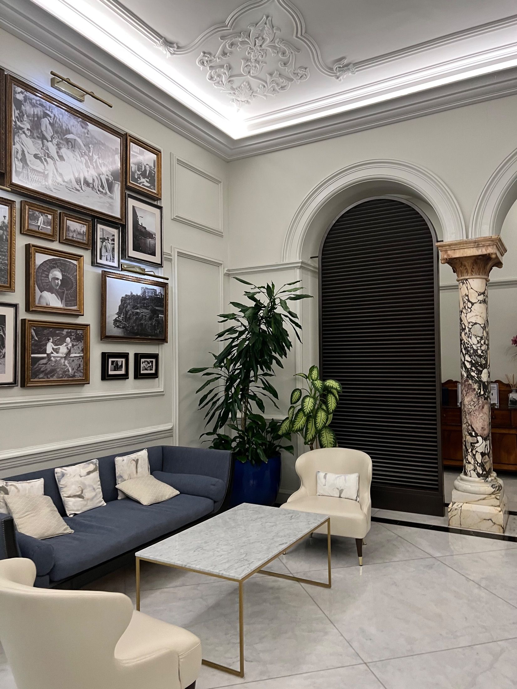 Seating area with blue sofa, cream armchairs, framed photographs and decorative ceiling plasterwork