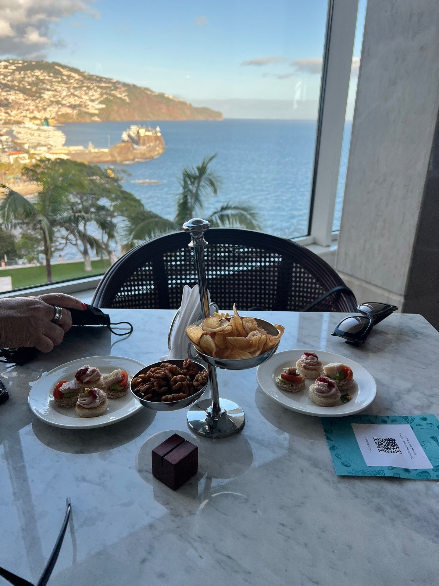 Afternoon tea canapes, crisps and nuts on a marble table with views over Funchal harbour at Reids Palace Champagne Bar, Madeira