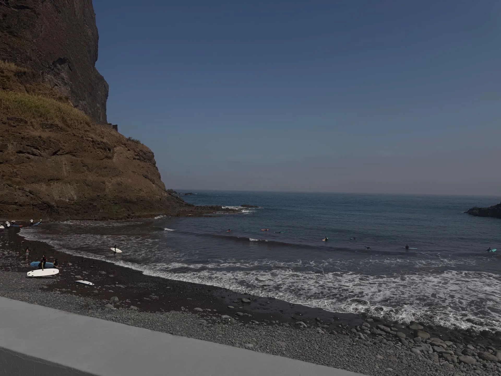 Surfers entering the water beside the volcanic cliffs at Praia da Alagoa in Porto da Cruz.