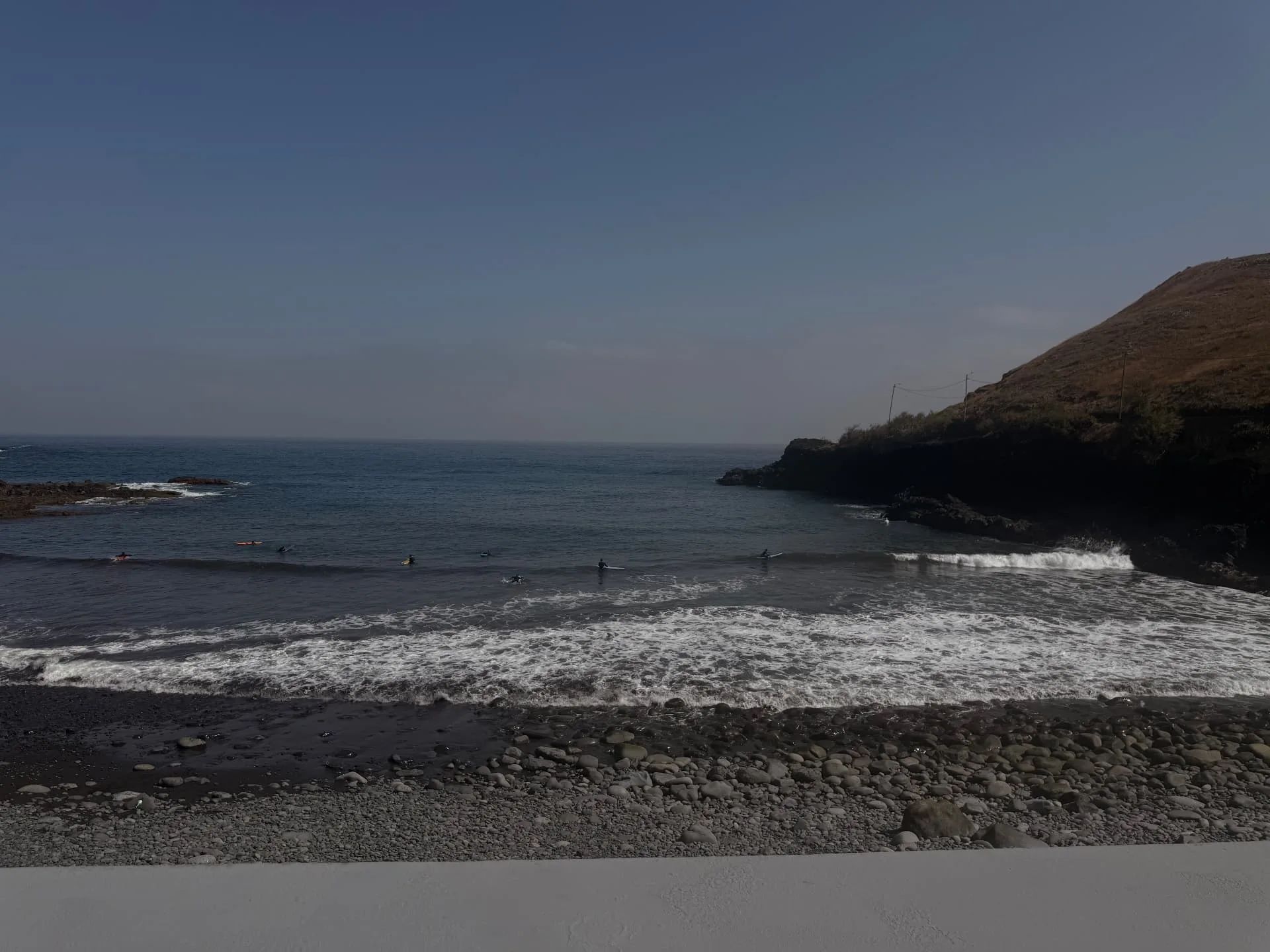 Surfers waiting for waves off Praia da Alagoa, Porto da Cruz, with the black pebble beach in the foreground.