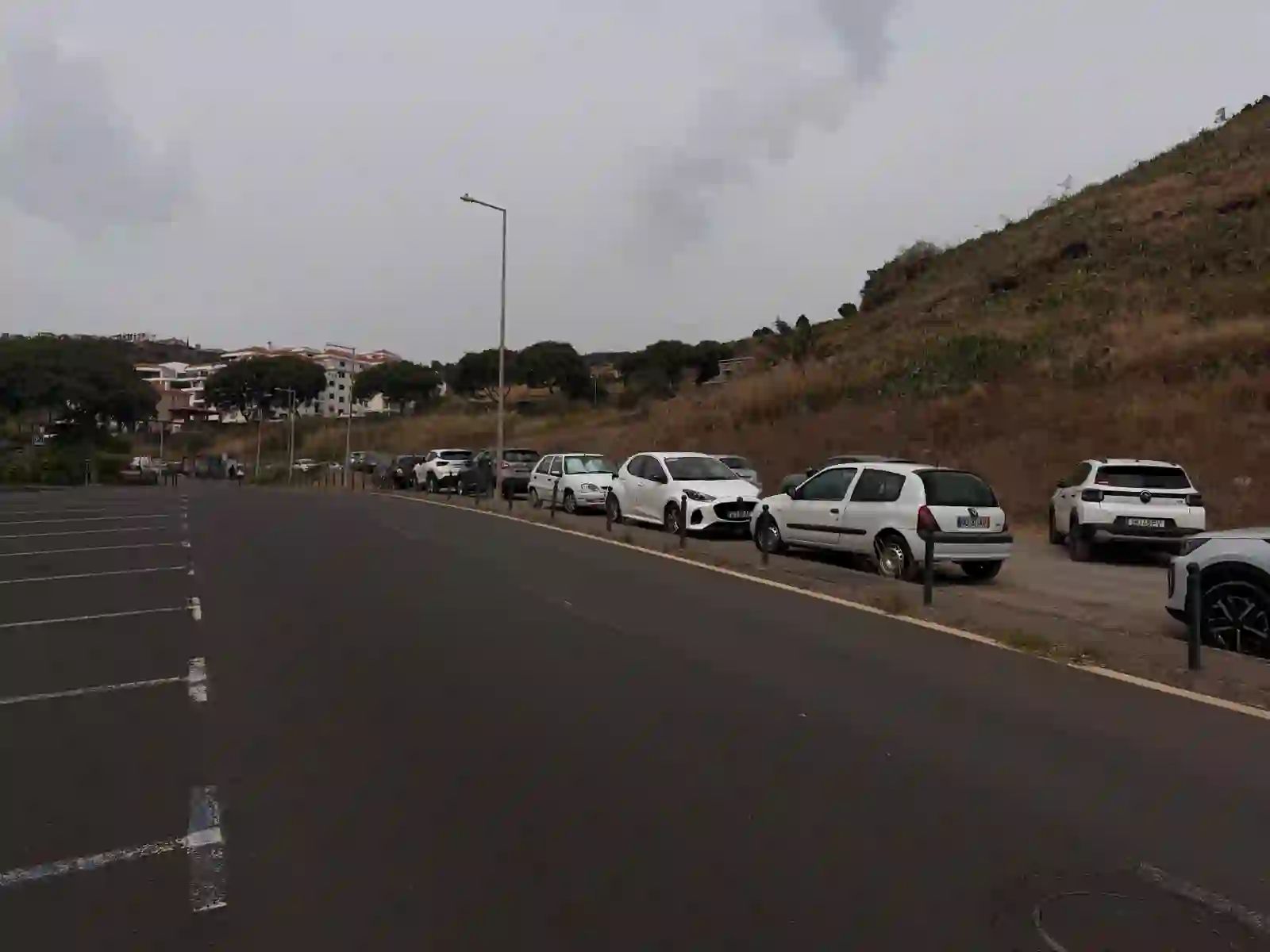 Cars parked along the road beside the free parking area at Reis Magos, Caniço de Baixo