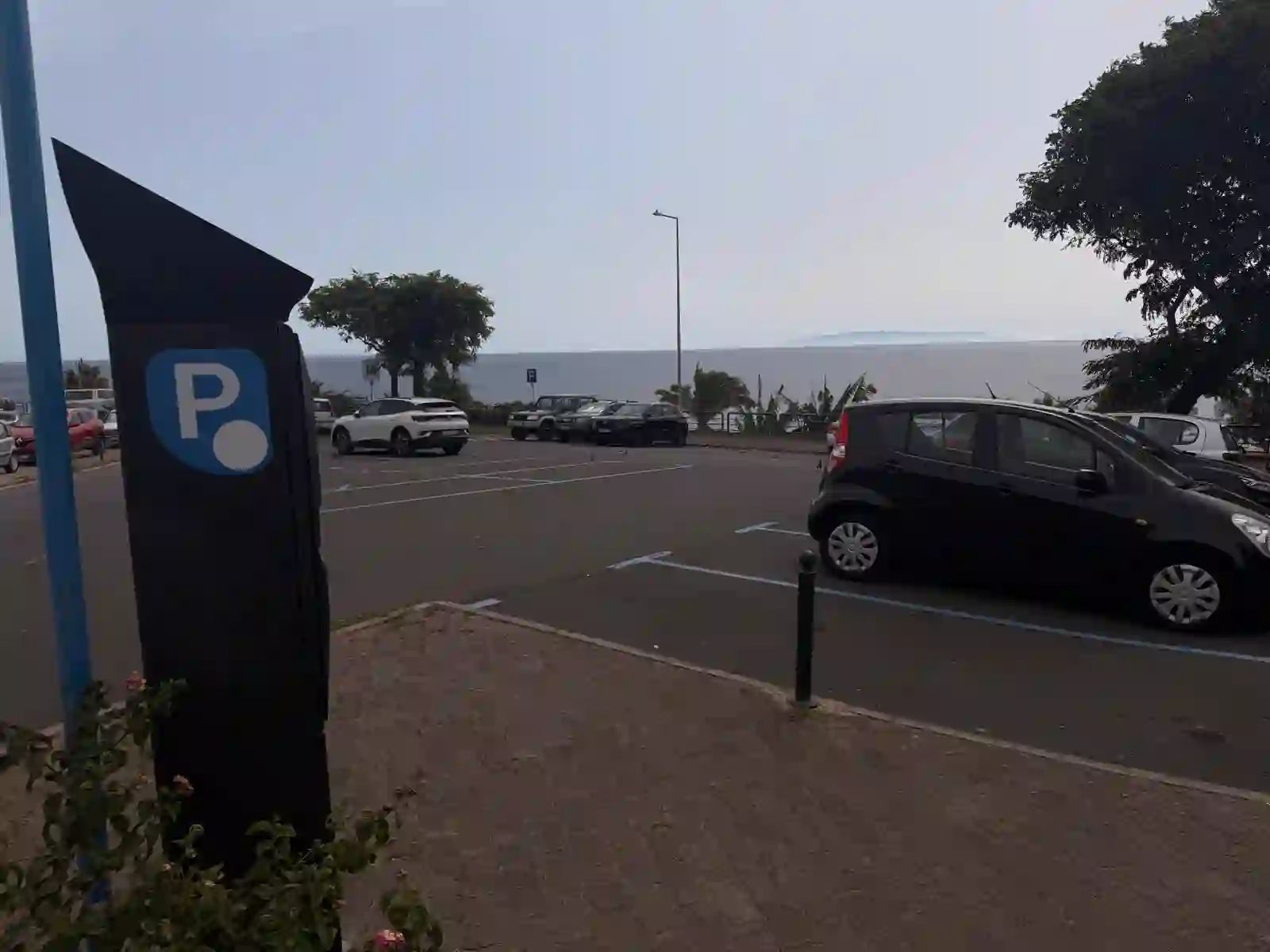 Paid parking meter and blue-lined bays on the seafront road at Praia dos Reis Magos