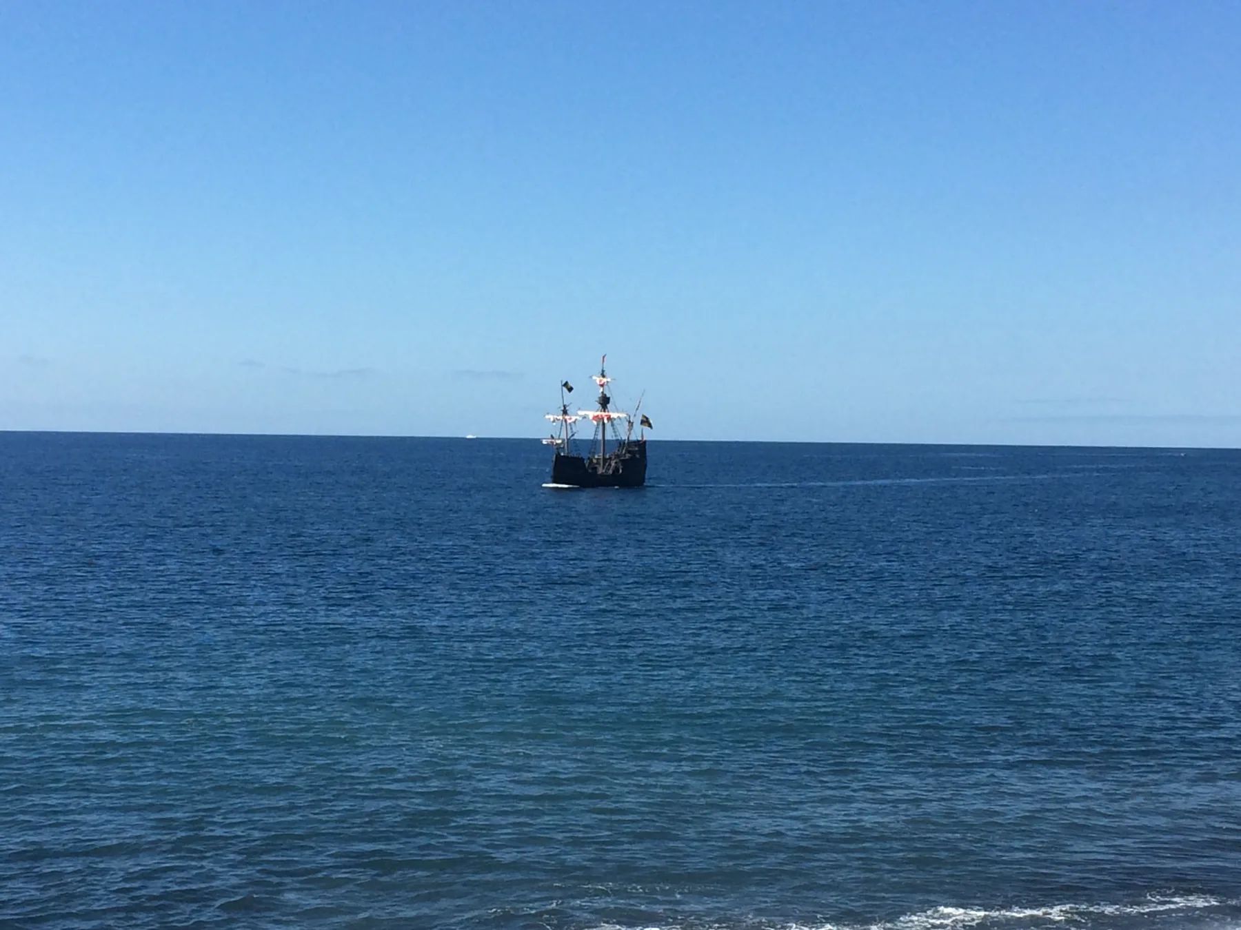 Santa Maria de Colombo replica ship sailing offshore from Praia Formosa beach, Madeira, under a clear blue sky