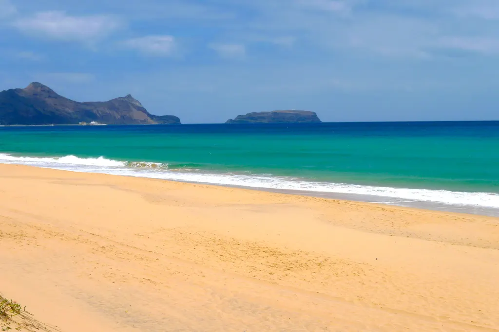 Golden sand and turquoise water at Porto Santo beach with the Ilhéu de Baixo islet on the horizon