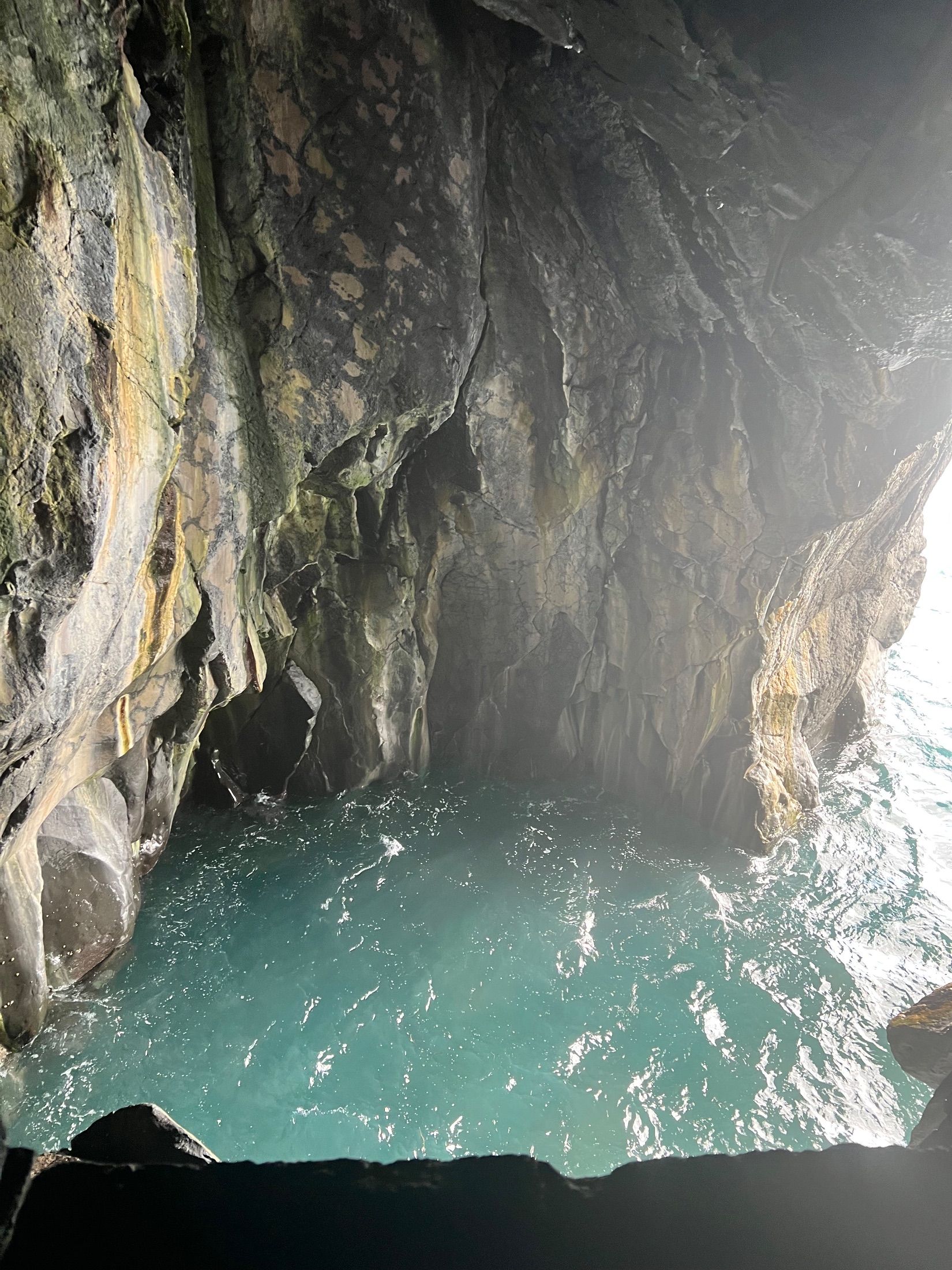 Turquoise seawater beneath steep, fissured rock walls in a shaded coastal recess