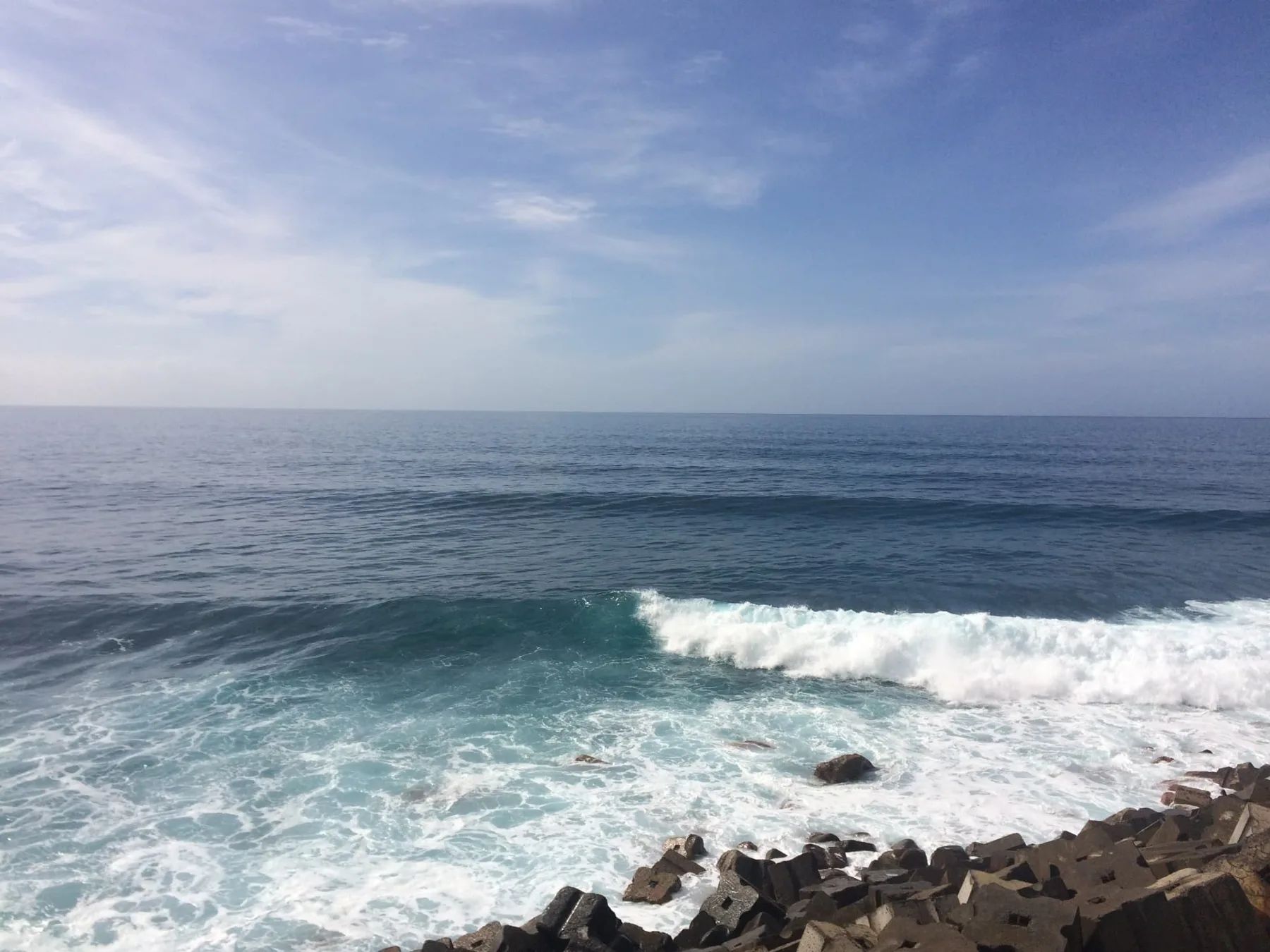 A wave breaking over the boulder shore at Jardim do Mar under a blue sky