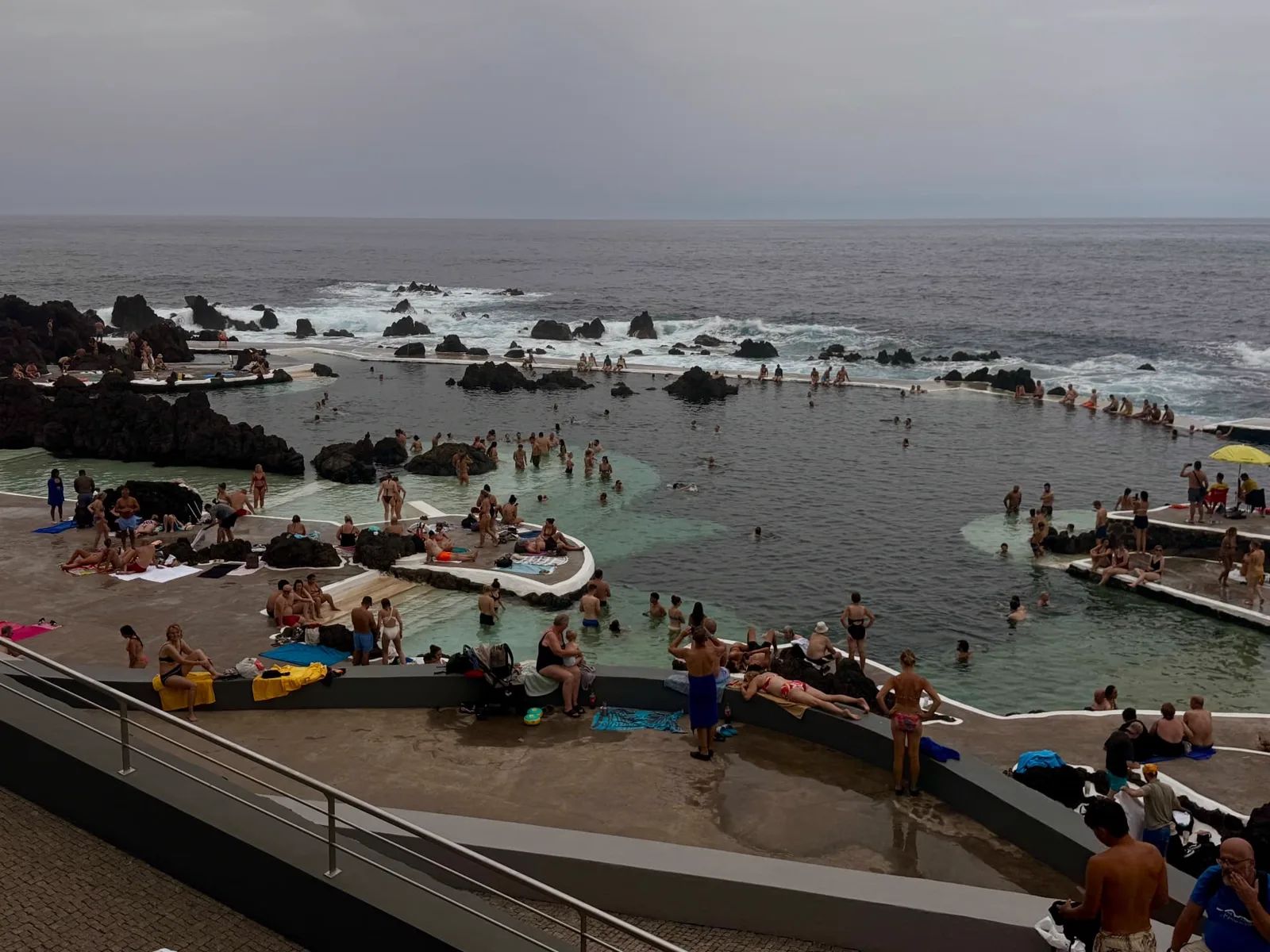 Swimmers in the Porto Moniz natural lava pools on a busy, overcast afternoon