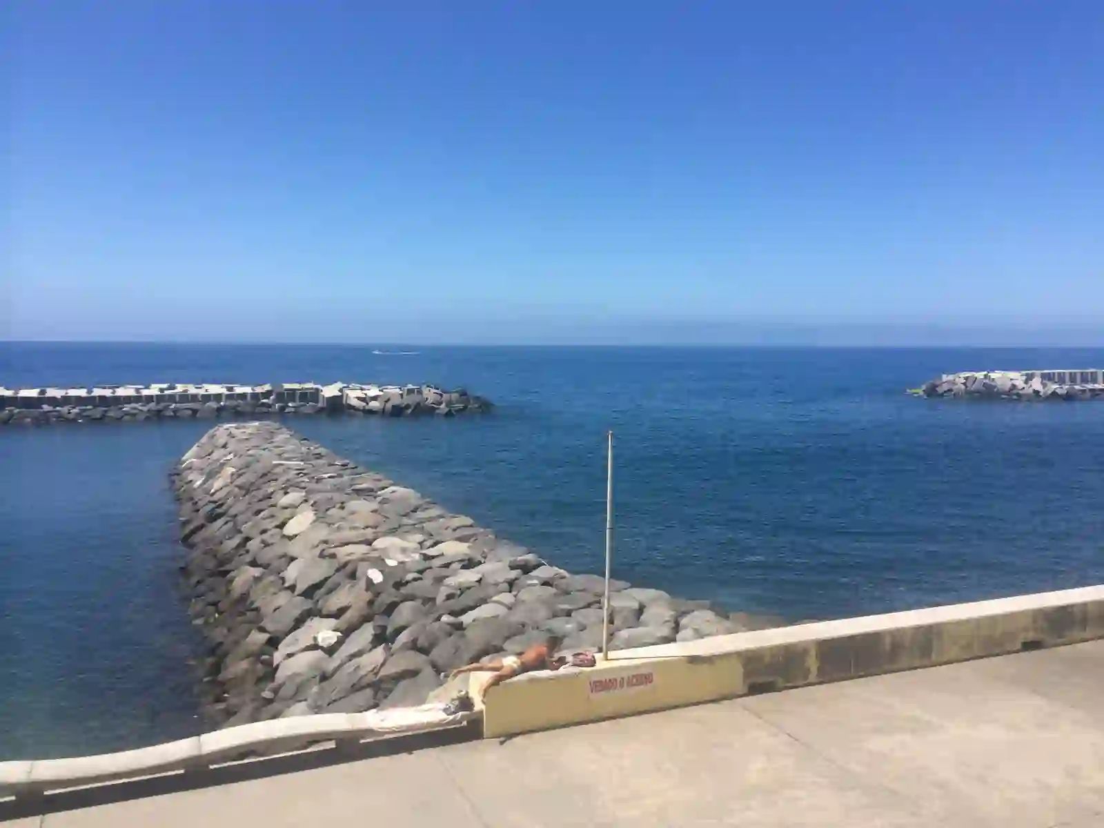 Breakwaters at Praia da Calheta with a sunbather on the wall