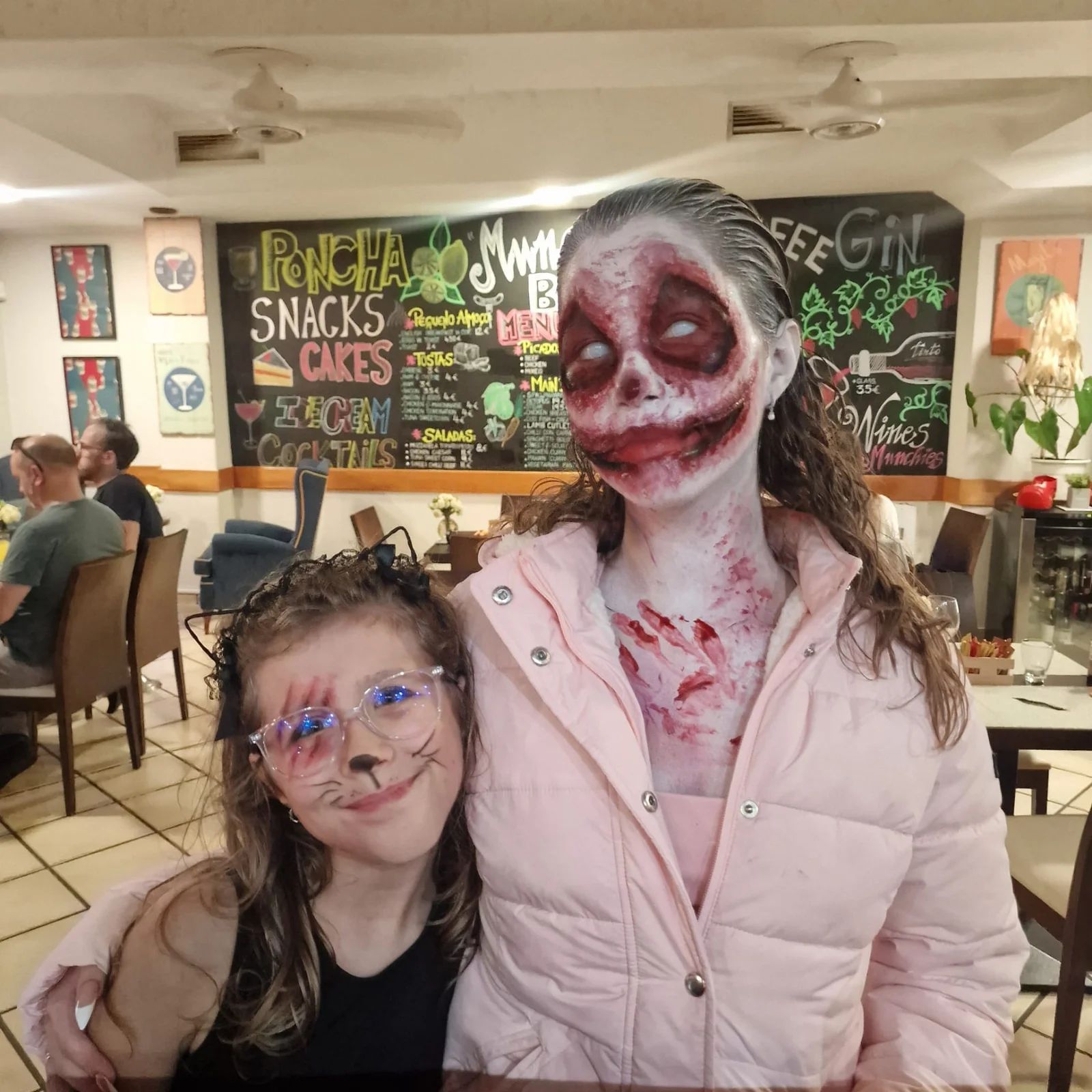 A woman with full zombie face paint and a child with cat makeup at Munchies in 2025