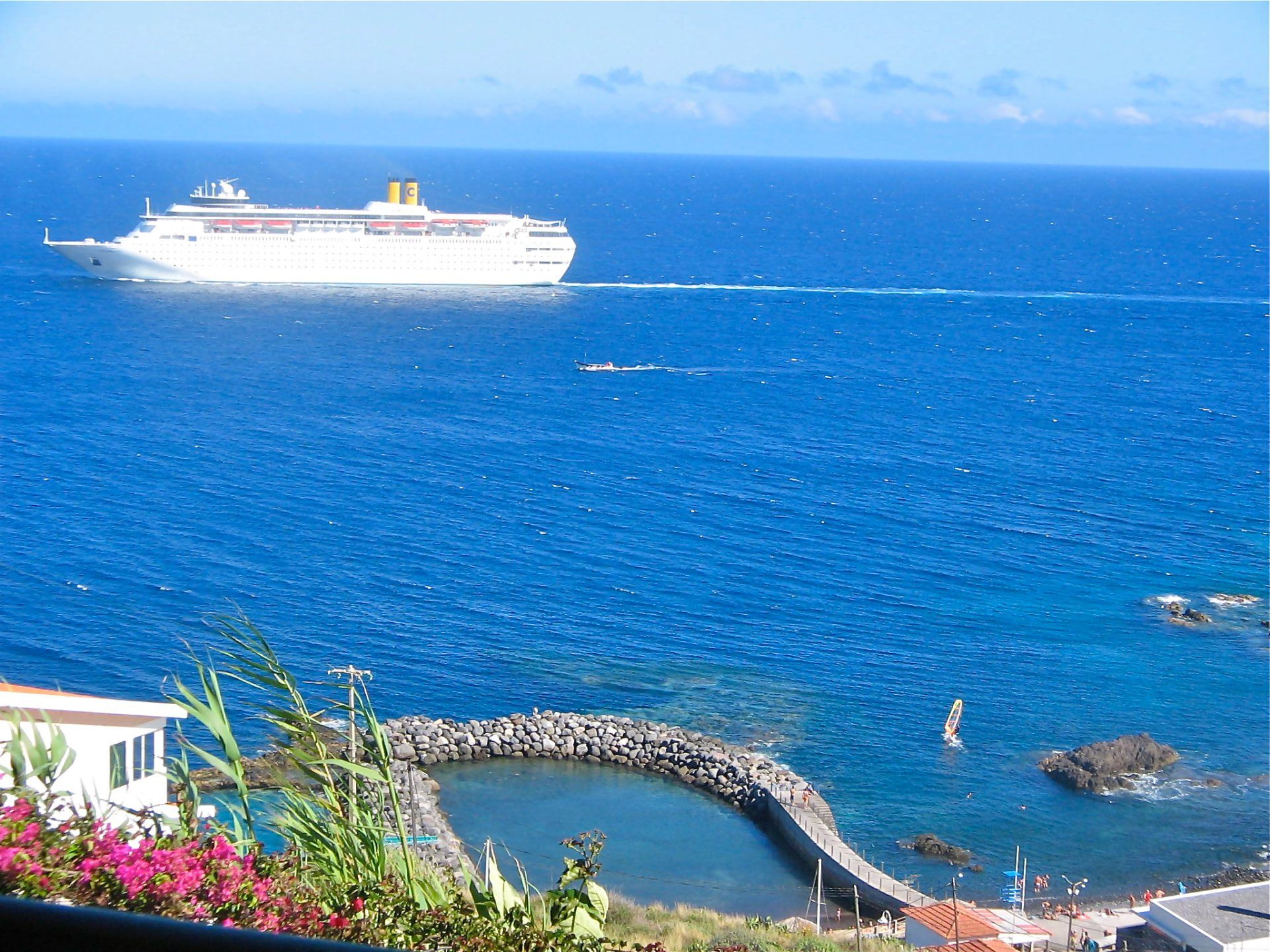 Cruise ship passing a rocky Madeira swimming area on a clear blue day.