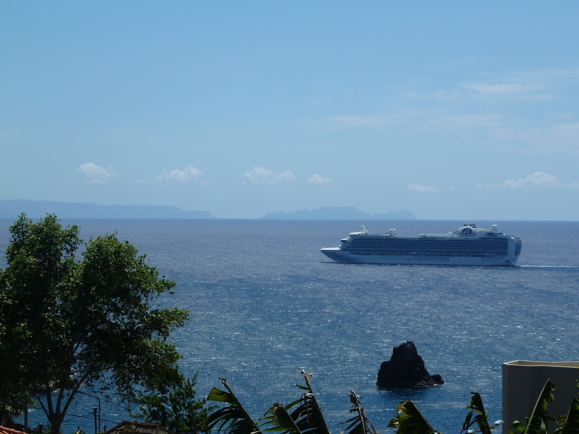 Cruise ship offshore with a rocky sea stack and distant islands.