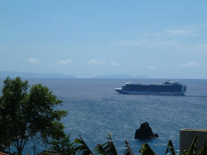 Cruise ship offshore with a rocky sea stack and distant islands.