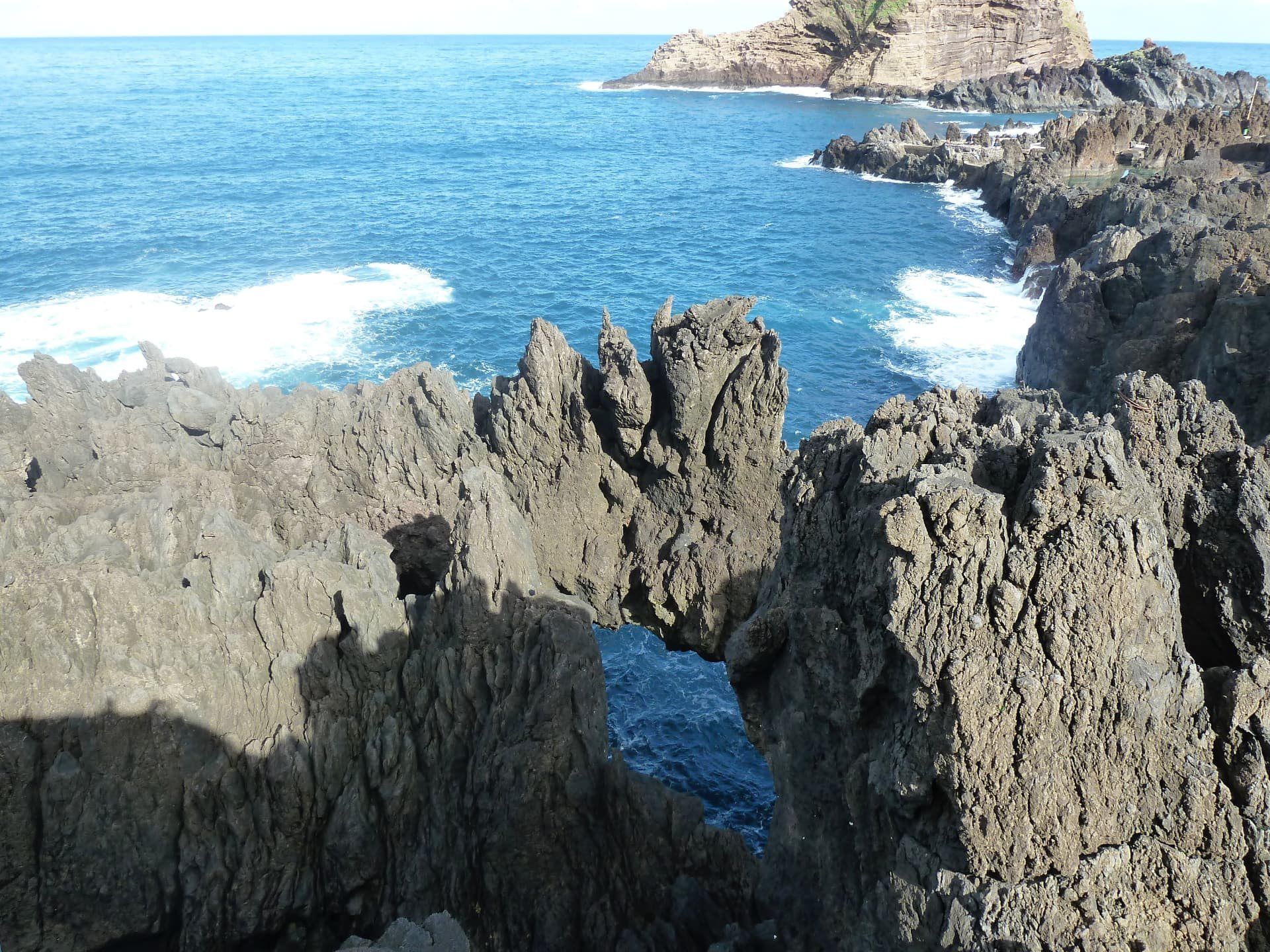 Rugged volcanic coastline with sea arches and breaking waves.