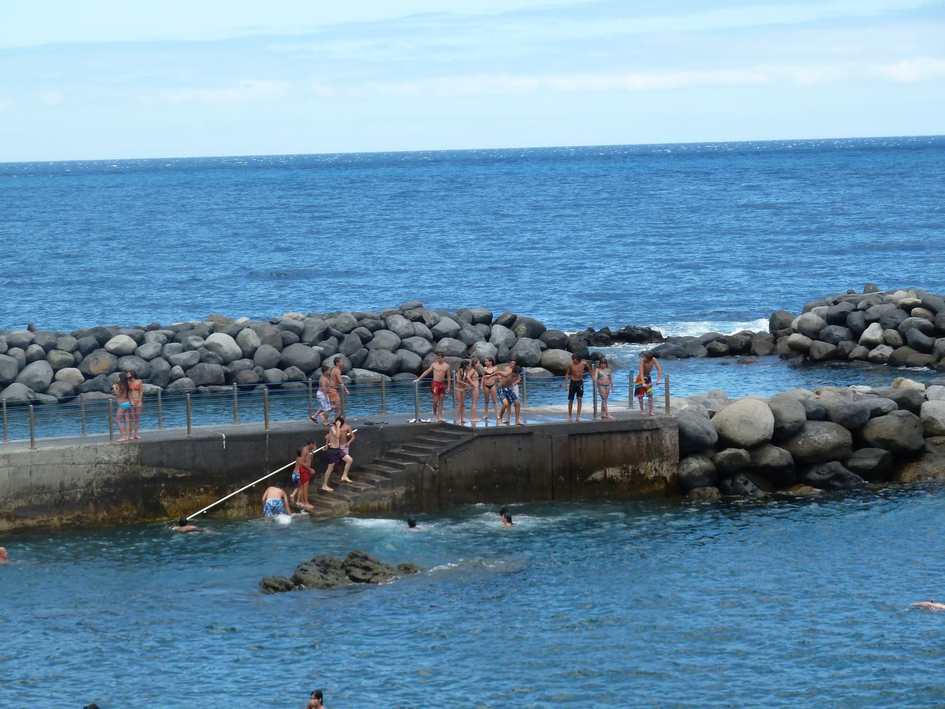Swimmers at a rocky Madeira ocean pool with concrete platforms and railings.