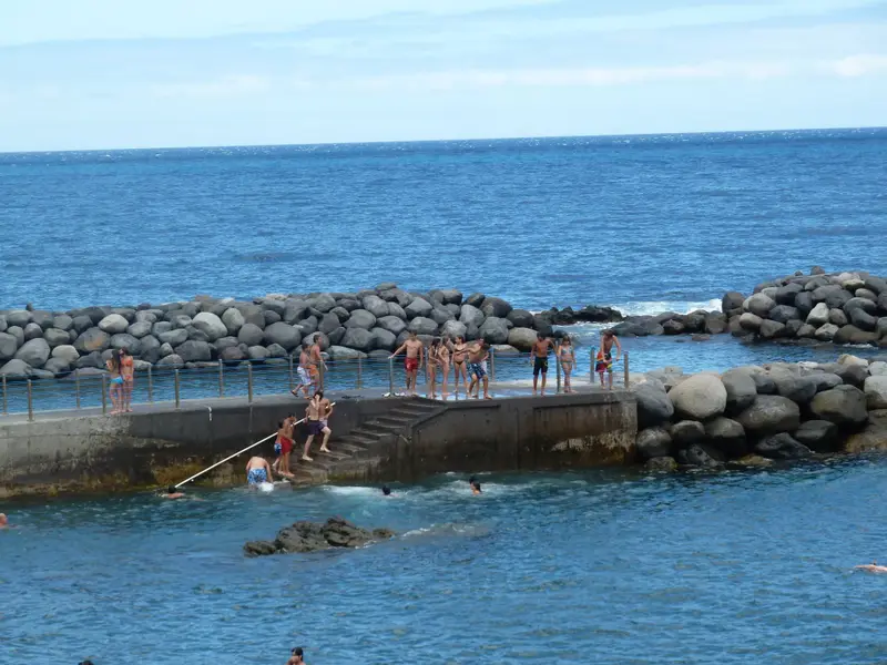 Swimmers at a rocky Madeira ocean pool with concrete platforms and railings.